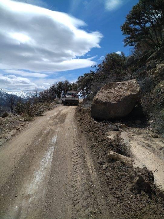 a large boulders sits on the road edge, and several inches of mud are covering the road after heavy winter rains.