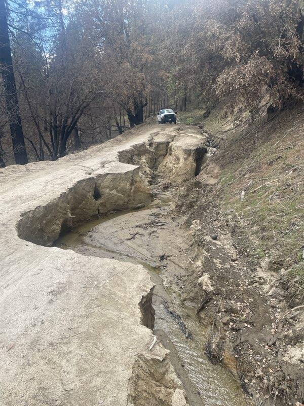 photo shows a gravel road with a deep erosion channel making the road impassable
