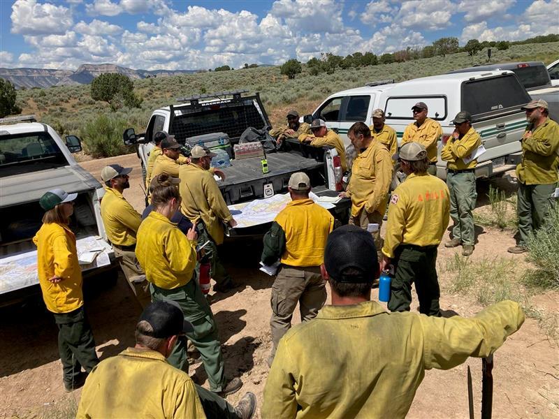 firefighters gather around a pickup truck tailgate to look at a map and talk