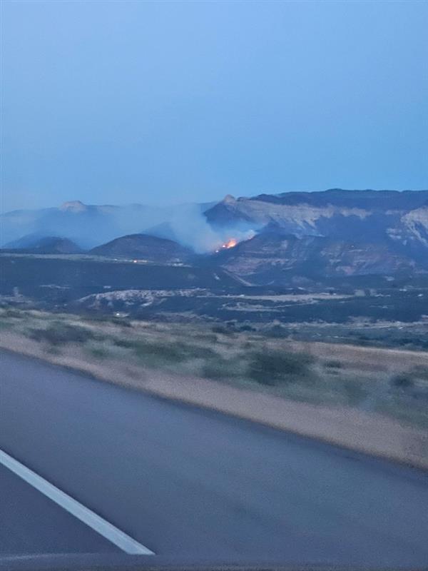 Light smoke and fire on hillside as seen from the paved road