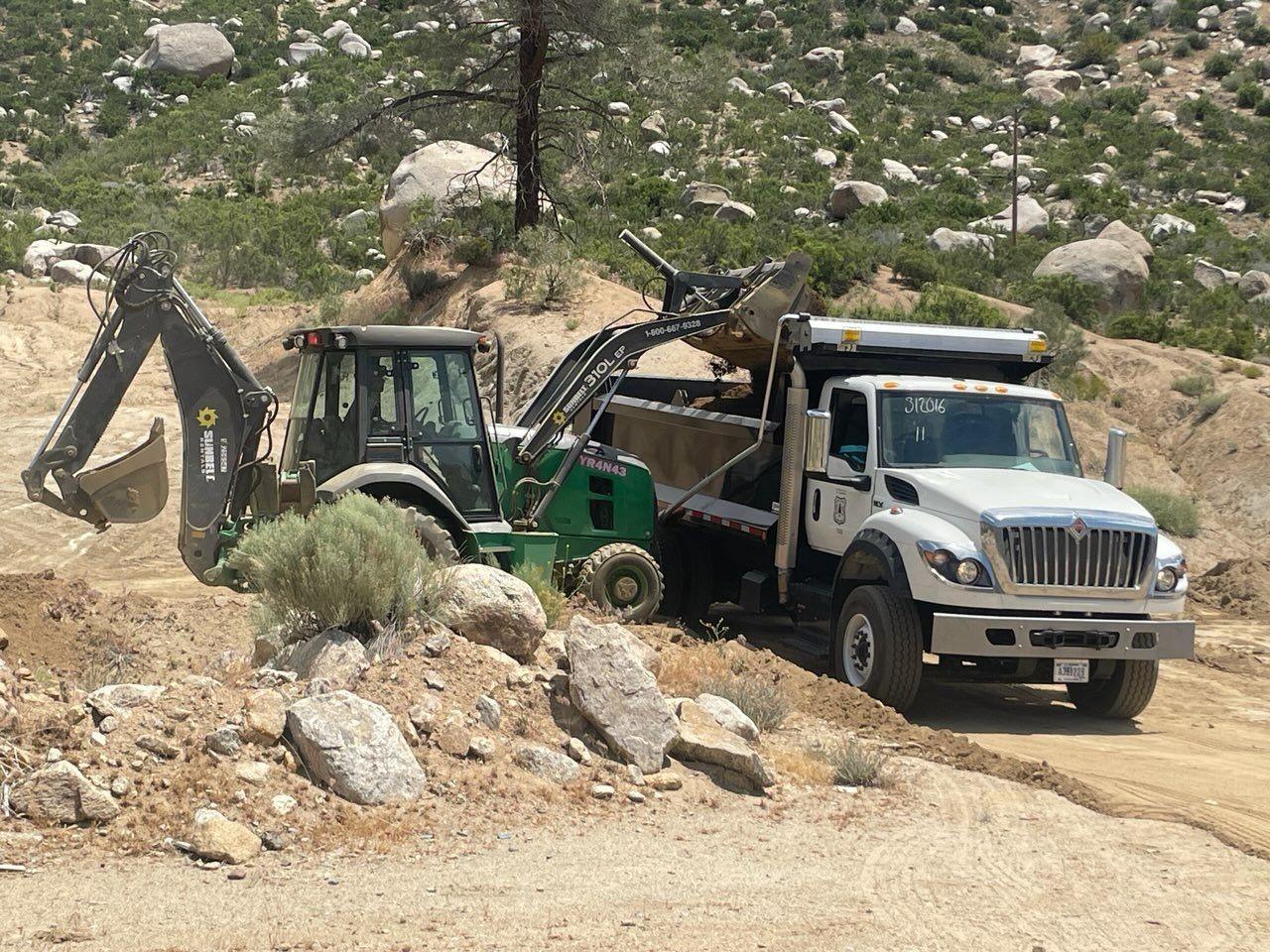 A tractor loads fill material into a dump truck