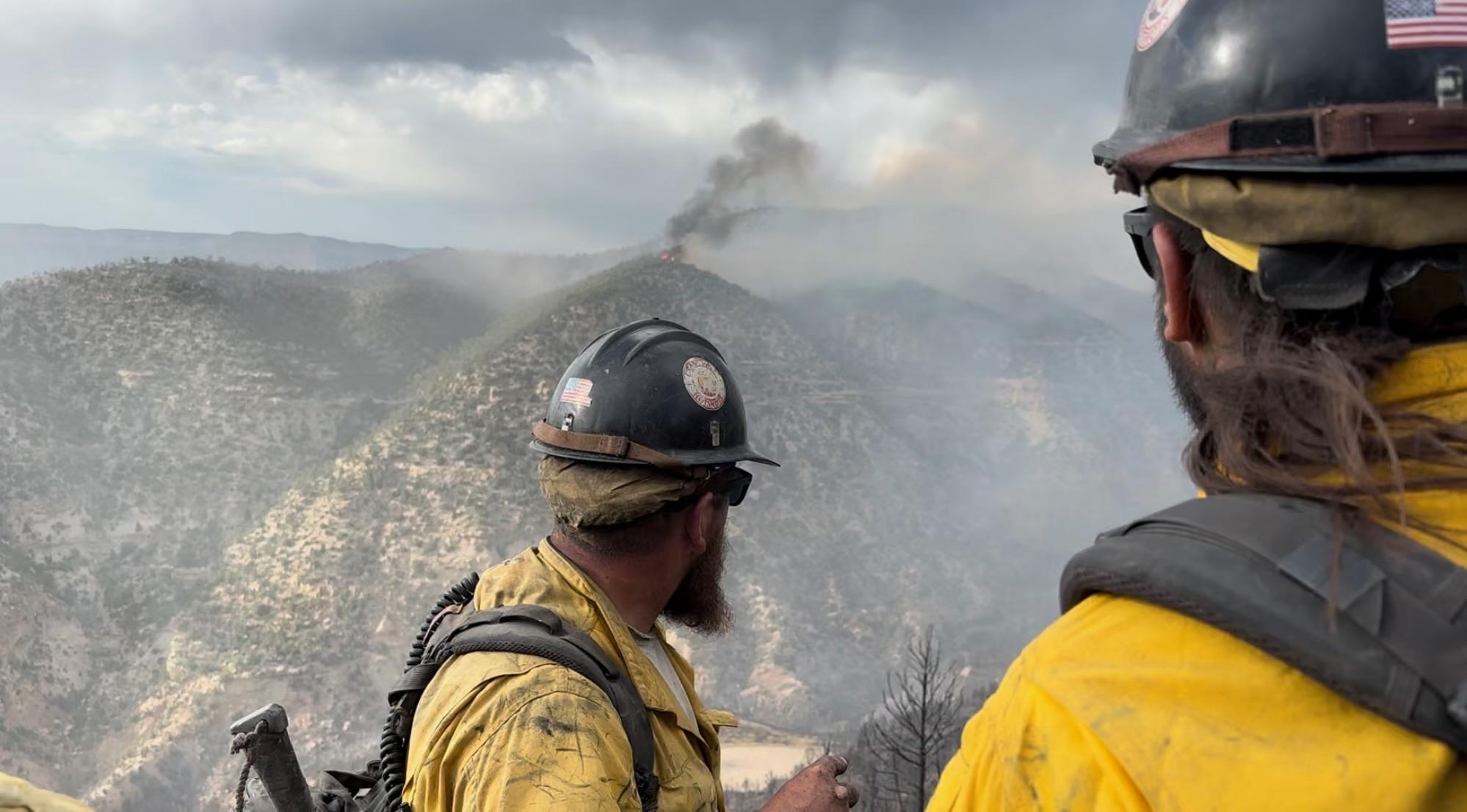 2 firefighters look at smoke on top of a distant mountain
