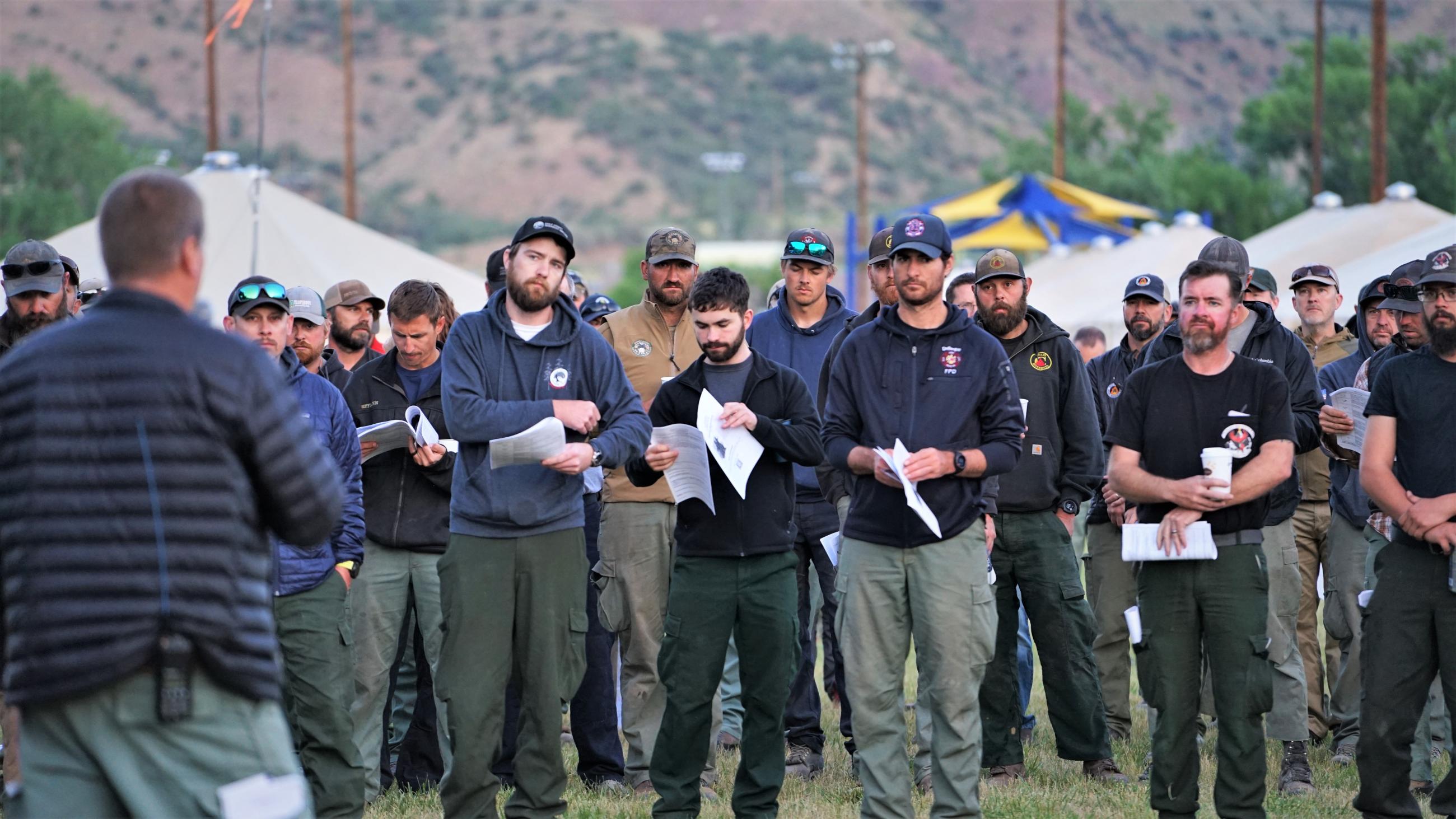 Tired firefighters listen to morning briefing Thursday, July 6