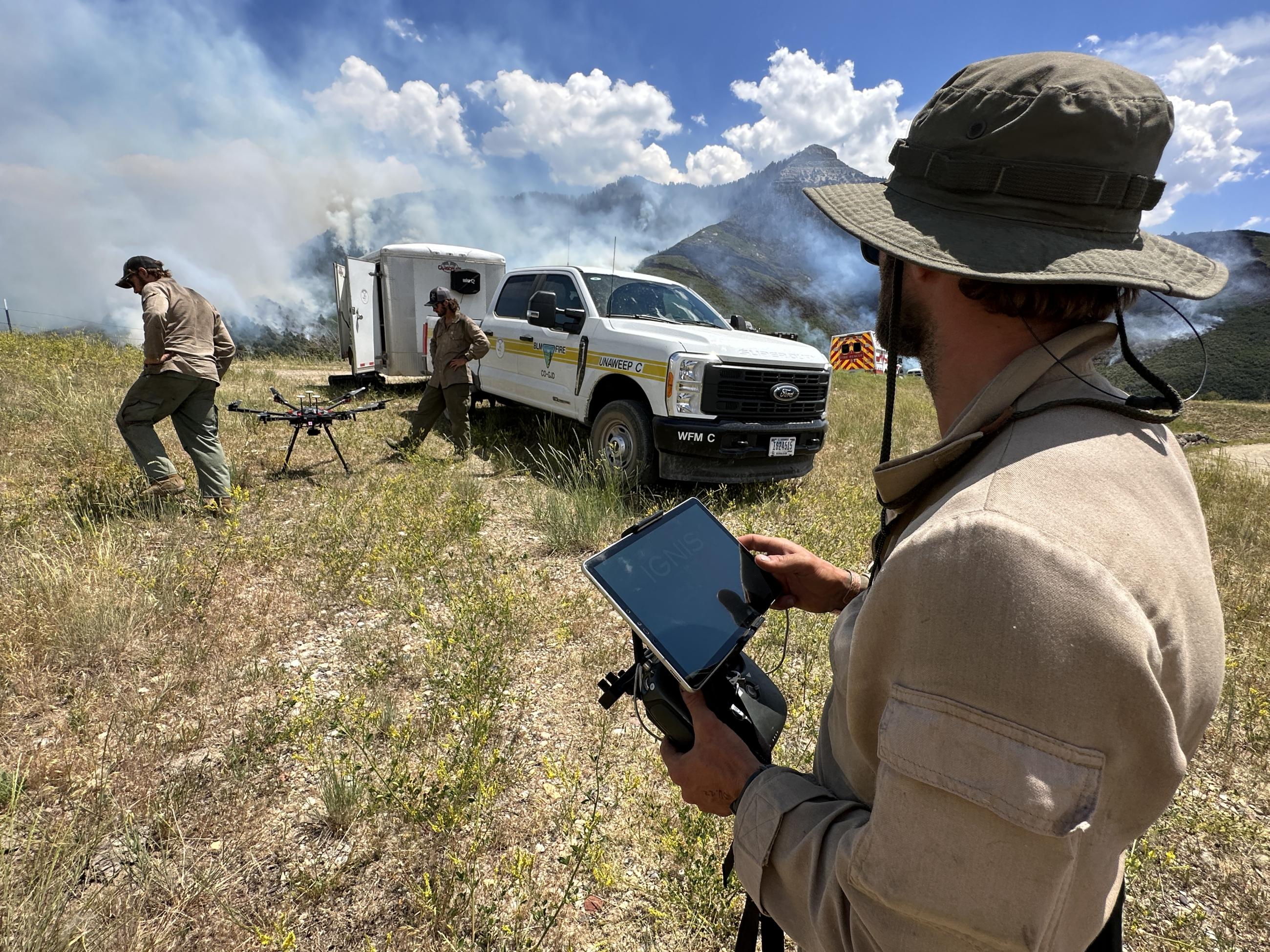 Drone personnel with drone on ground and smoke in background