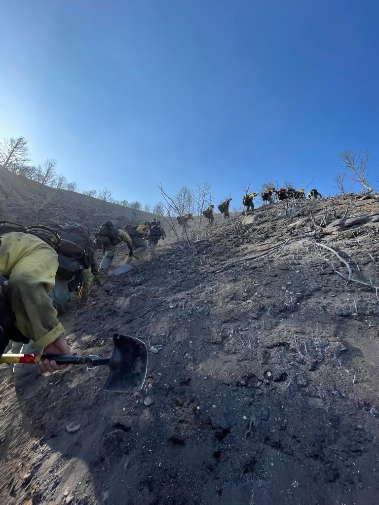 firefighters hike up a steep slope on the south side of the fire