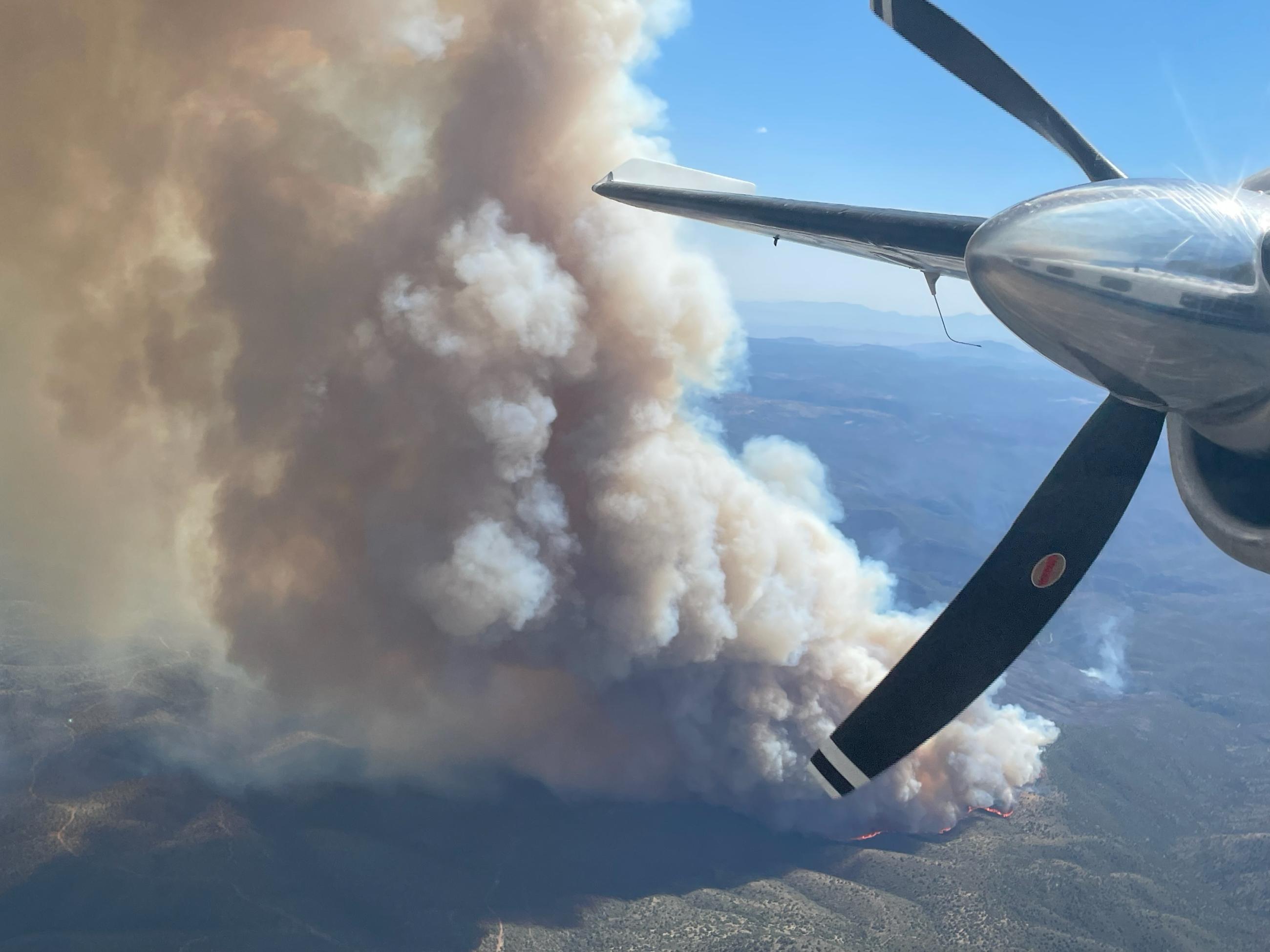 Aerial view of Spoon fire with large smoke plume and visible flames in background with aircraft propeller in foreground