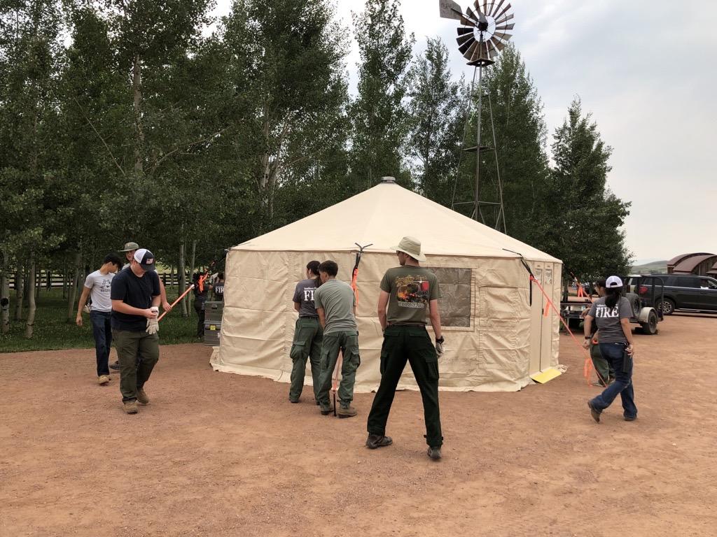Several camp crew workers are at work setting up a beige tent also known as a yurt.