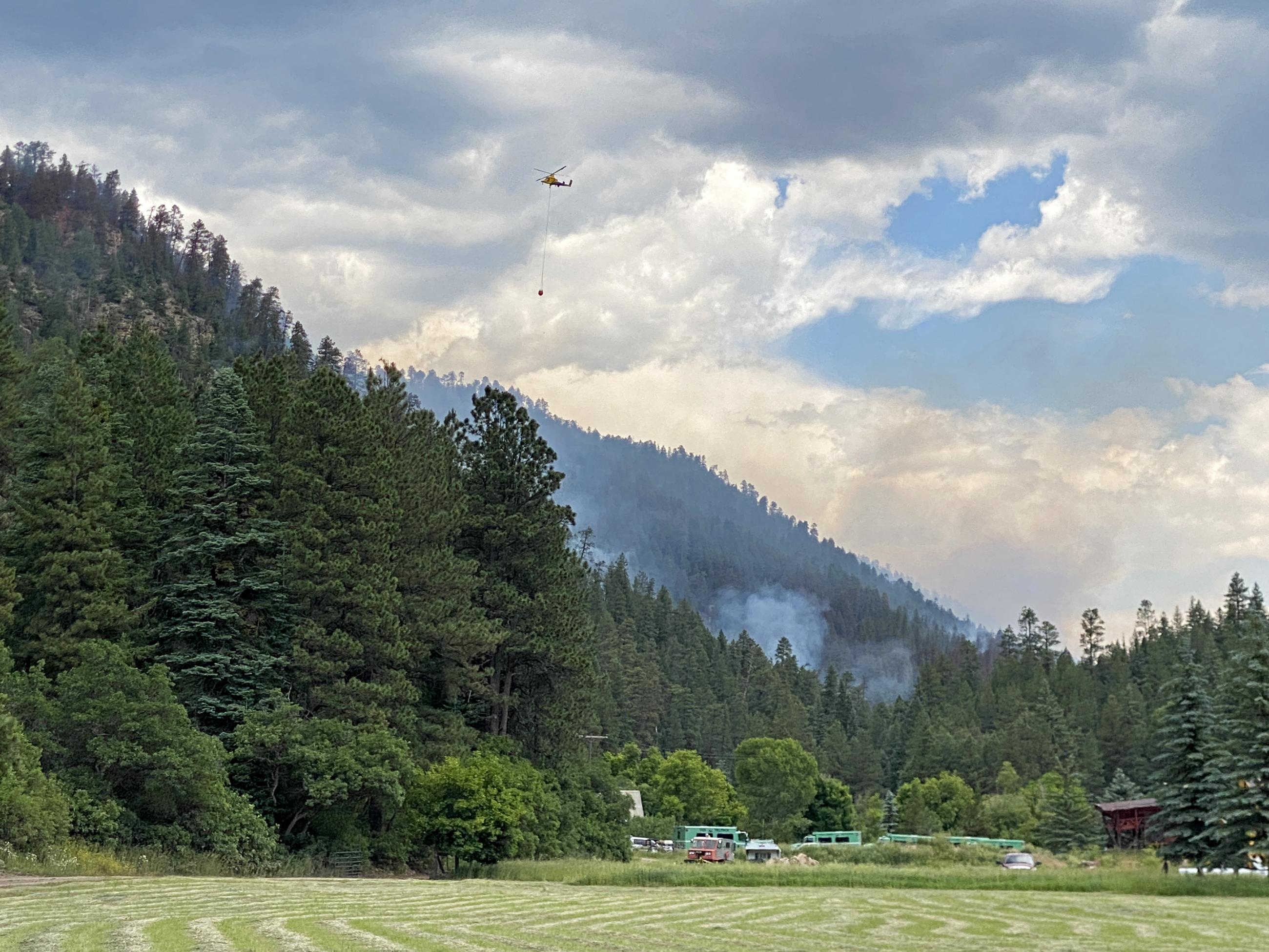 View of Snow Angel Ranch with moderate backing fire on hillside and helicopter in left corner of photo