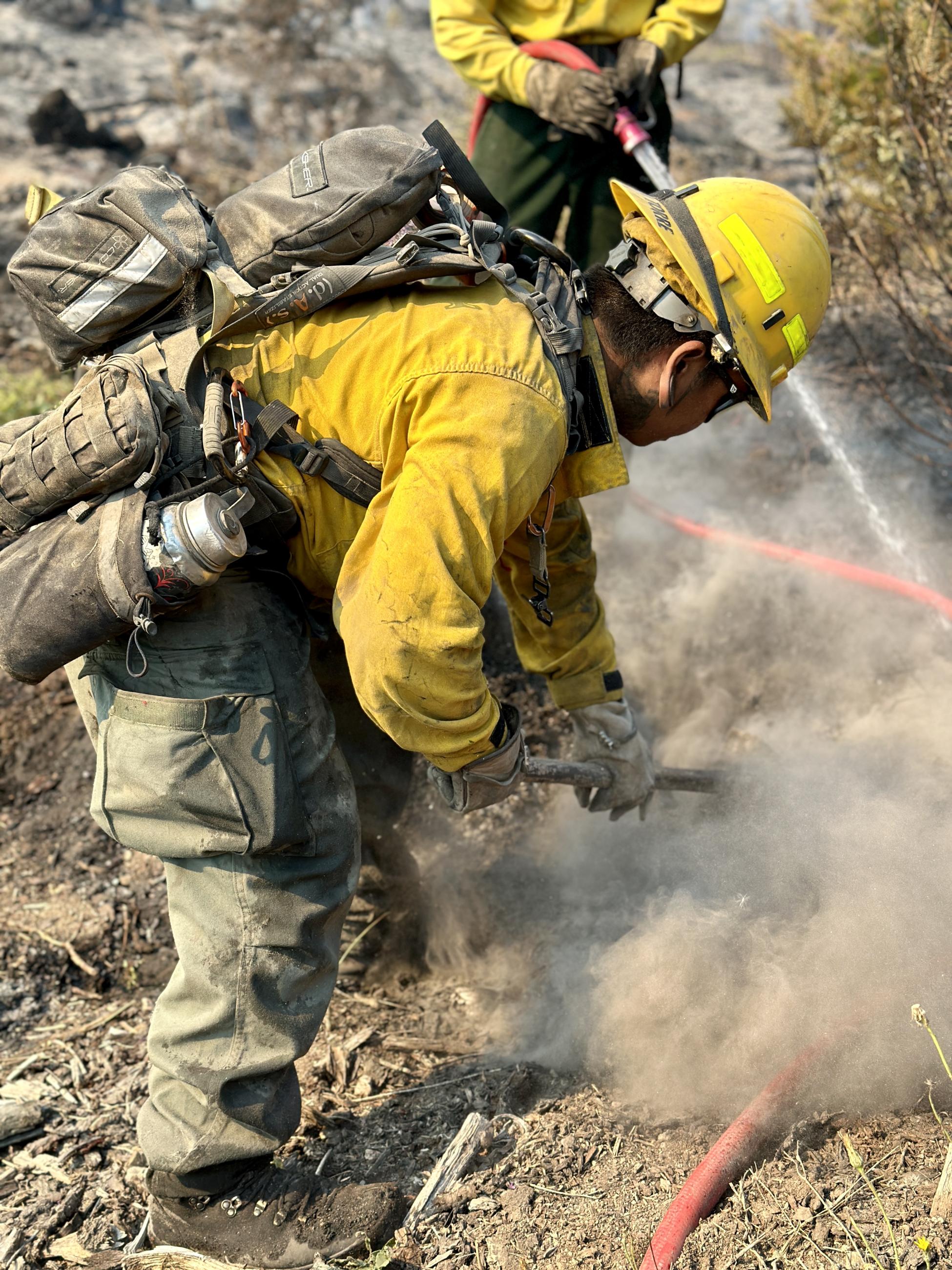A firefighter uses a pulaski to mop-up a hot spot.