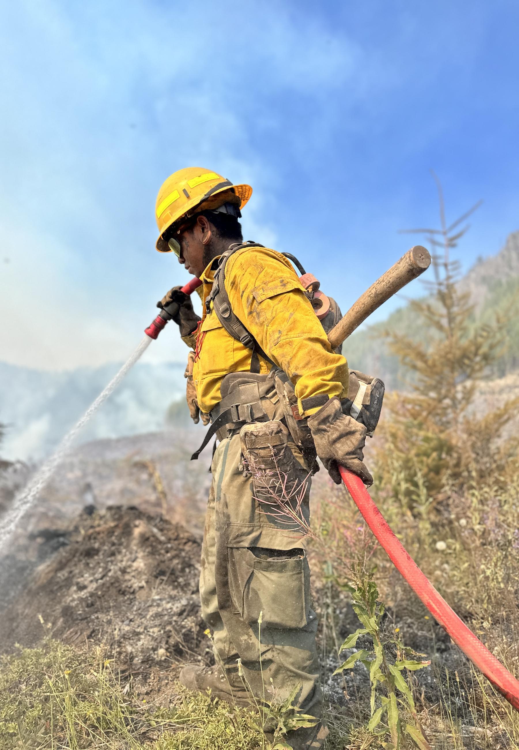 A firefighter uses a hose to mop-up a hot spot.