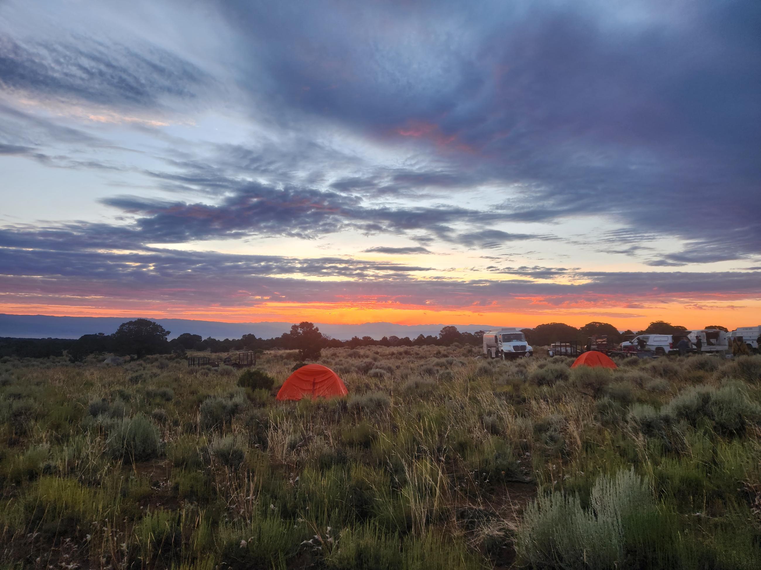 Image of beautiful sunset with orange and blue at the Little Mesa Fire spike camp with orange tents and fire vehicles