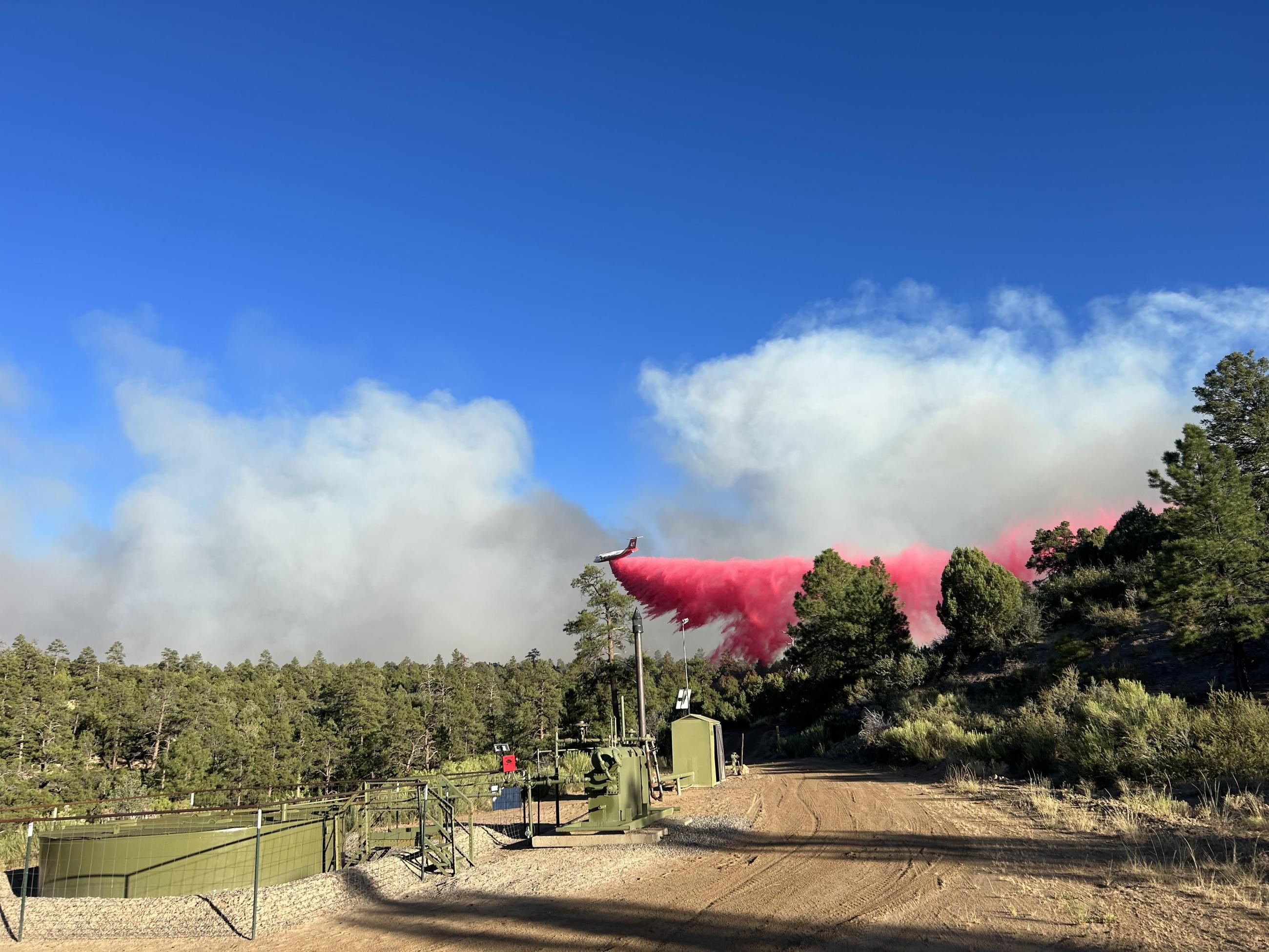A very large airtanker drops retardant on a area where smoke is rising.