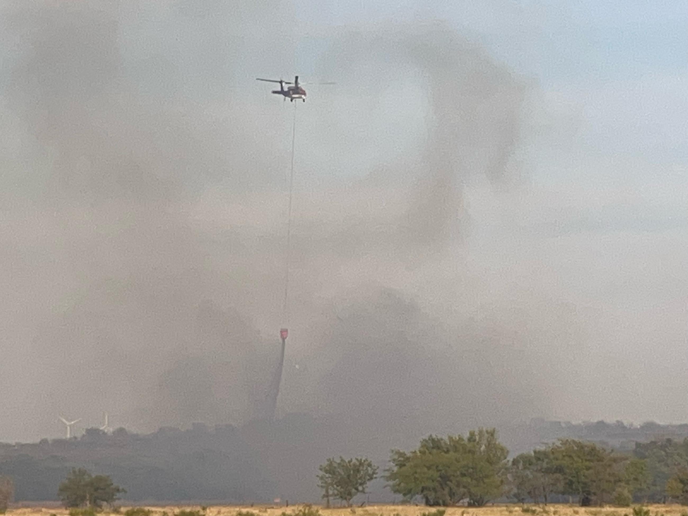 Helicopter making bucket drops on hotspots of the fire, helping crews hold the containment lines