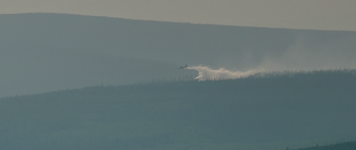 A plane drops water over smoky mountain and forest.