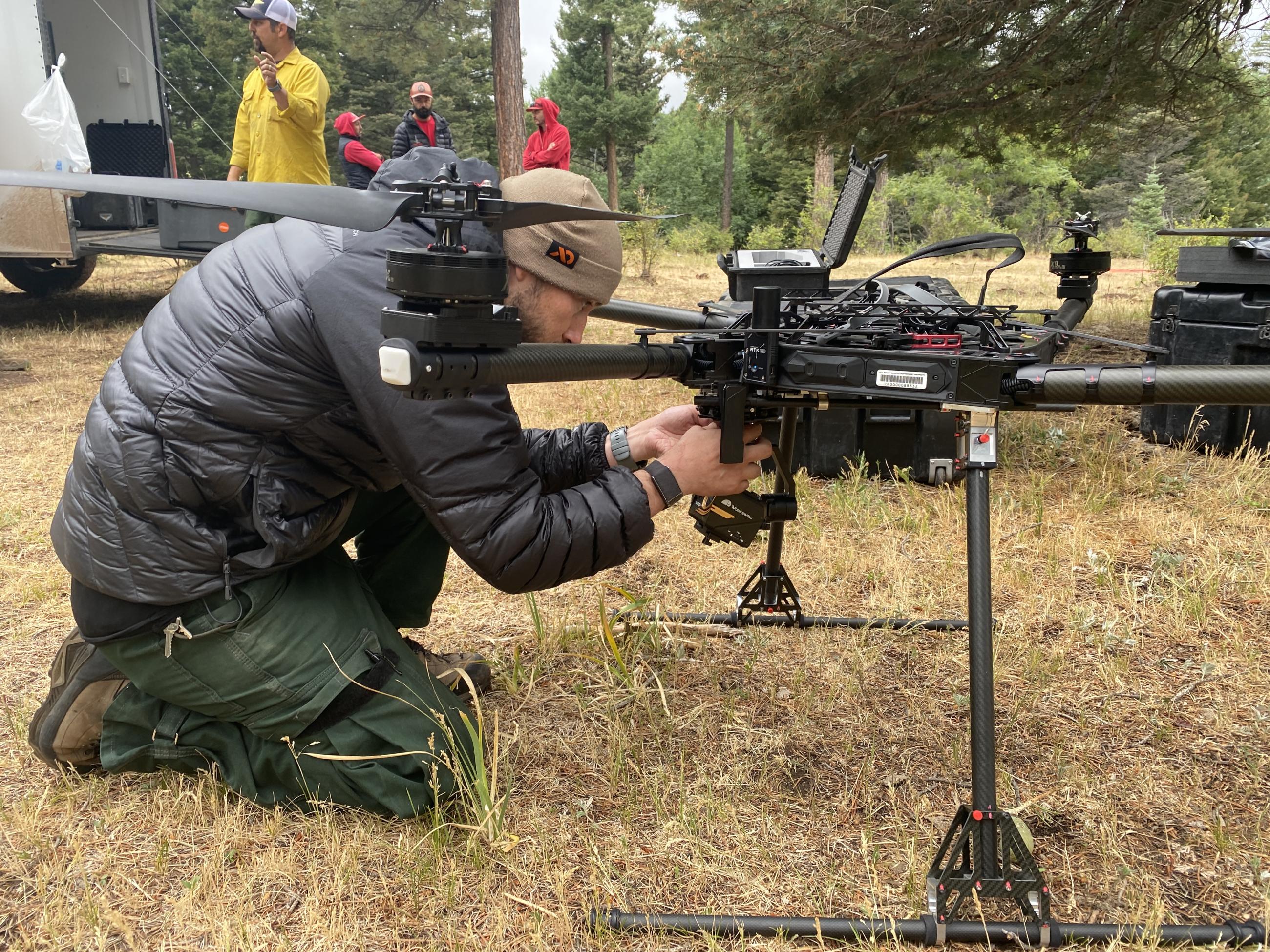 Image is a picture of a man kneeling next to a drone.