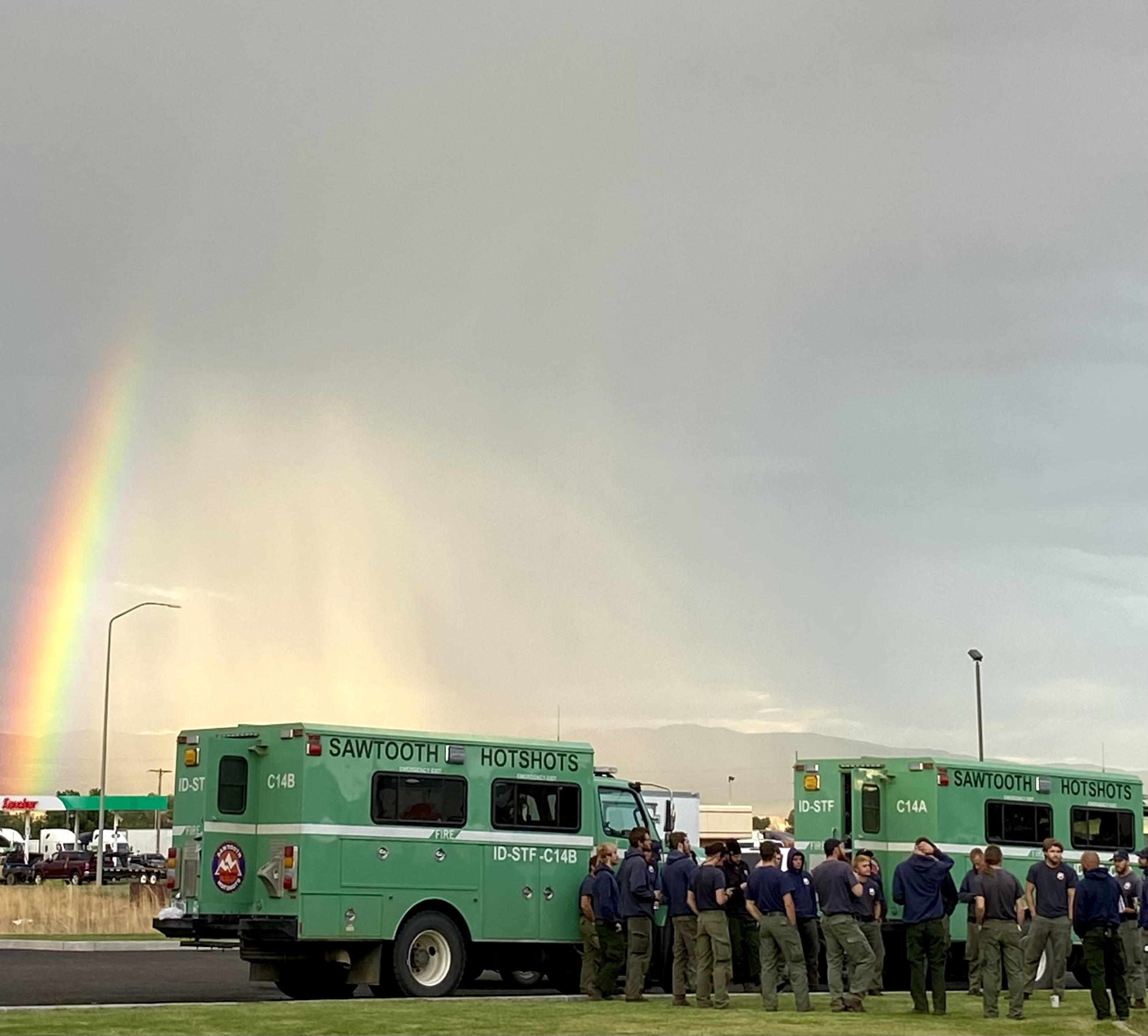Firefighters stand by their crew buggies with a rainbow overhead