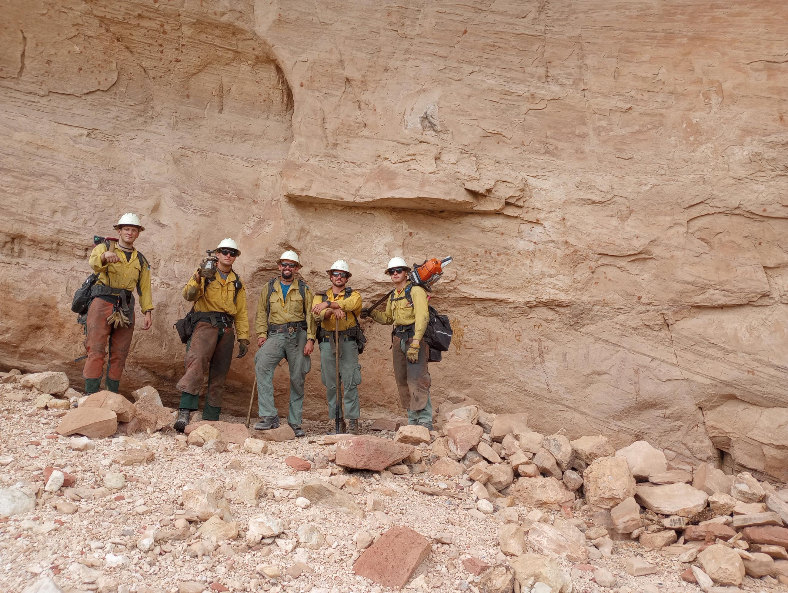 firefighters pose with rock writings  after removing vegetation thereby protecting them.