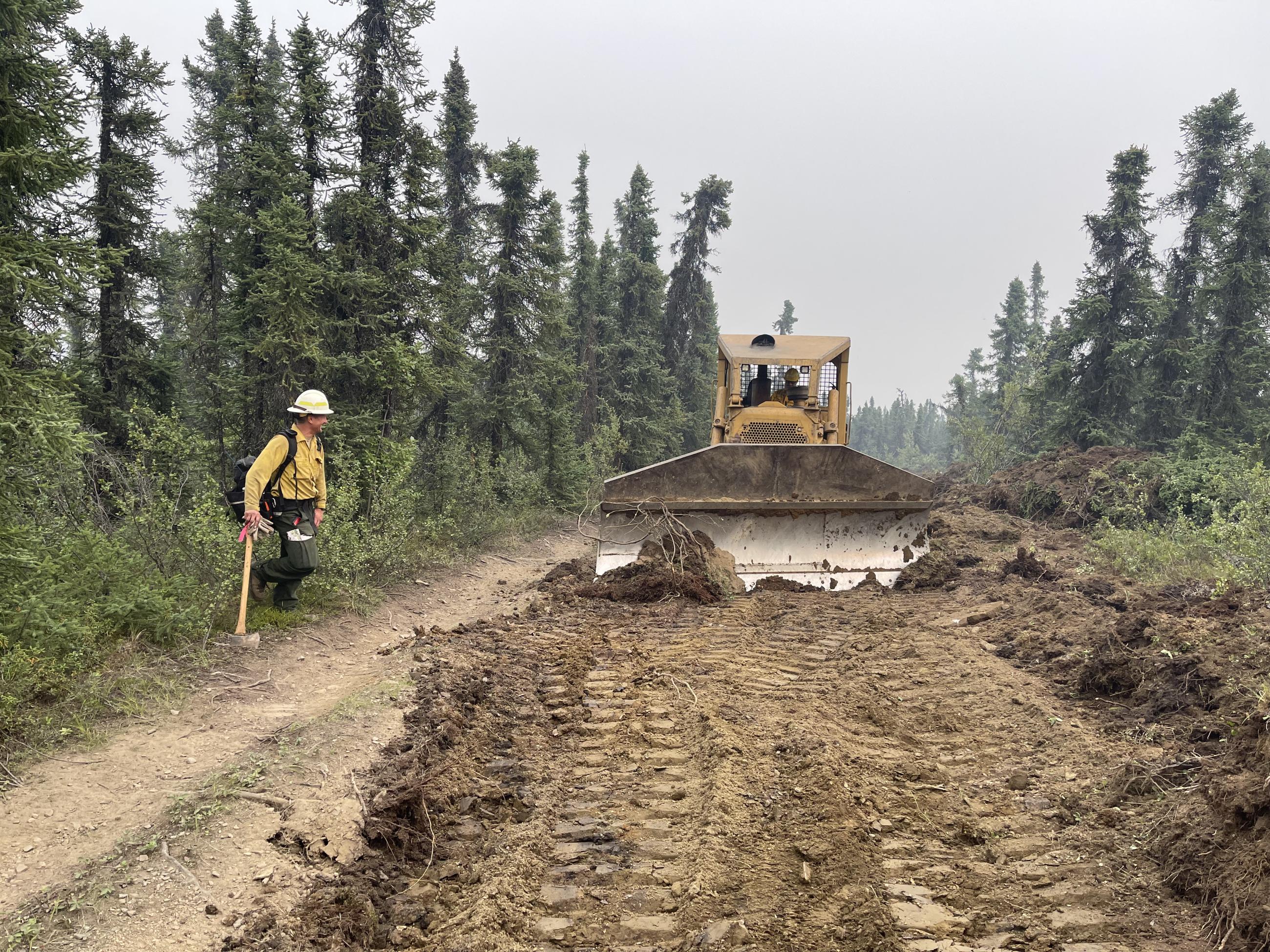 A bulldozer and firefighter work to create contingency line.