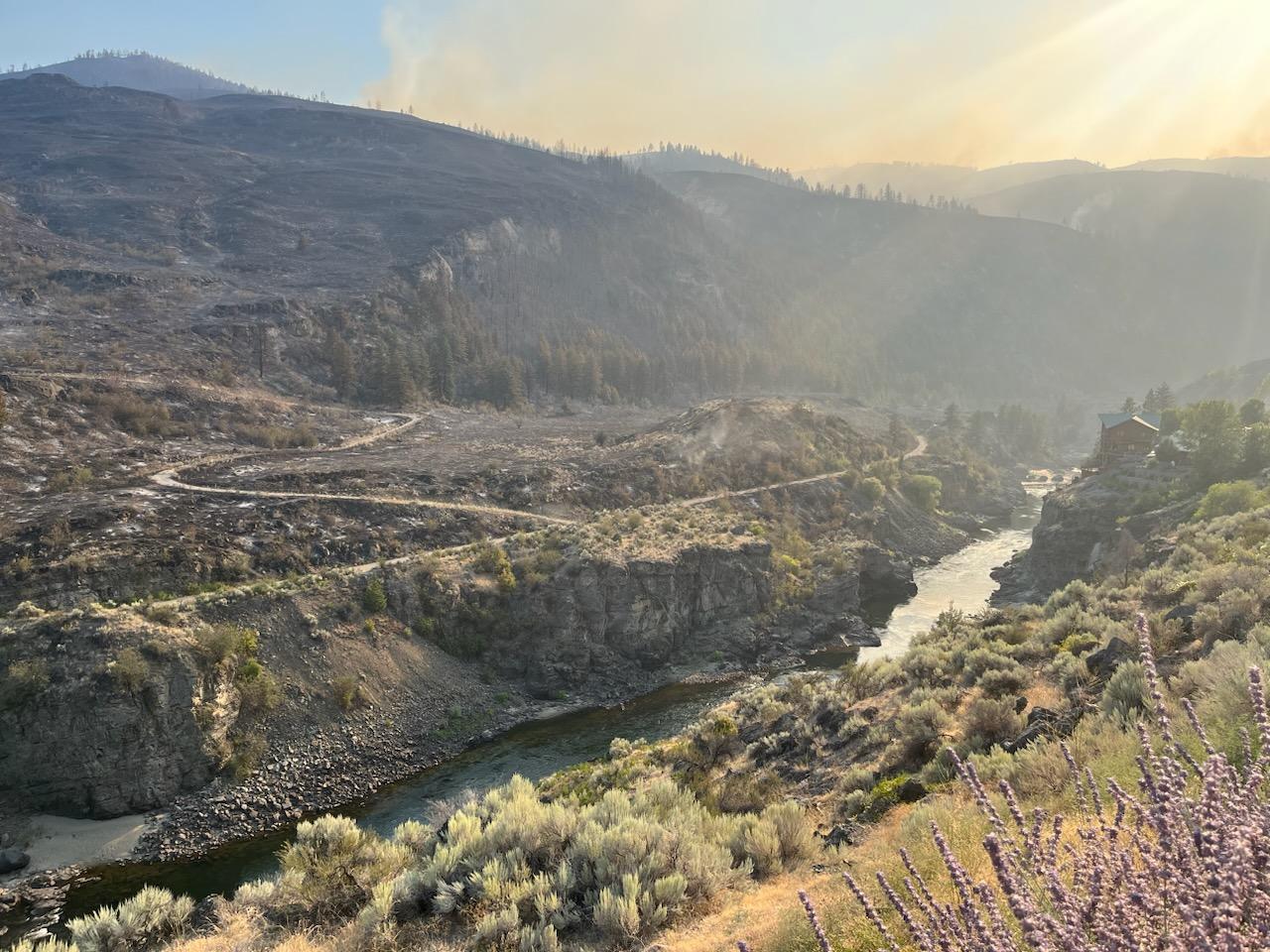 A burned landscape in the background with a home on the Similkameen River in the foreground