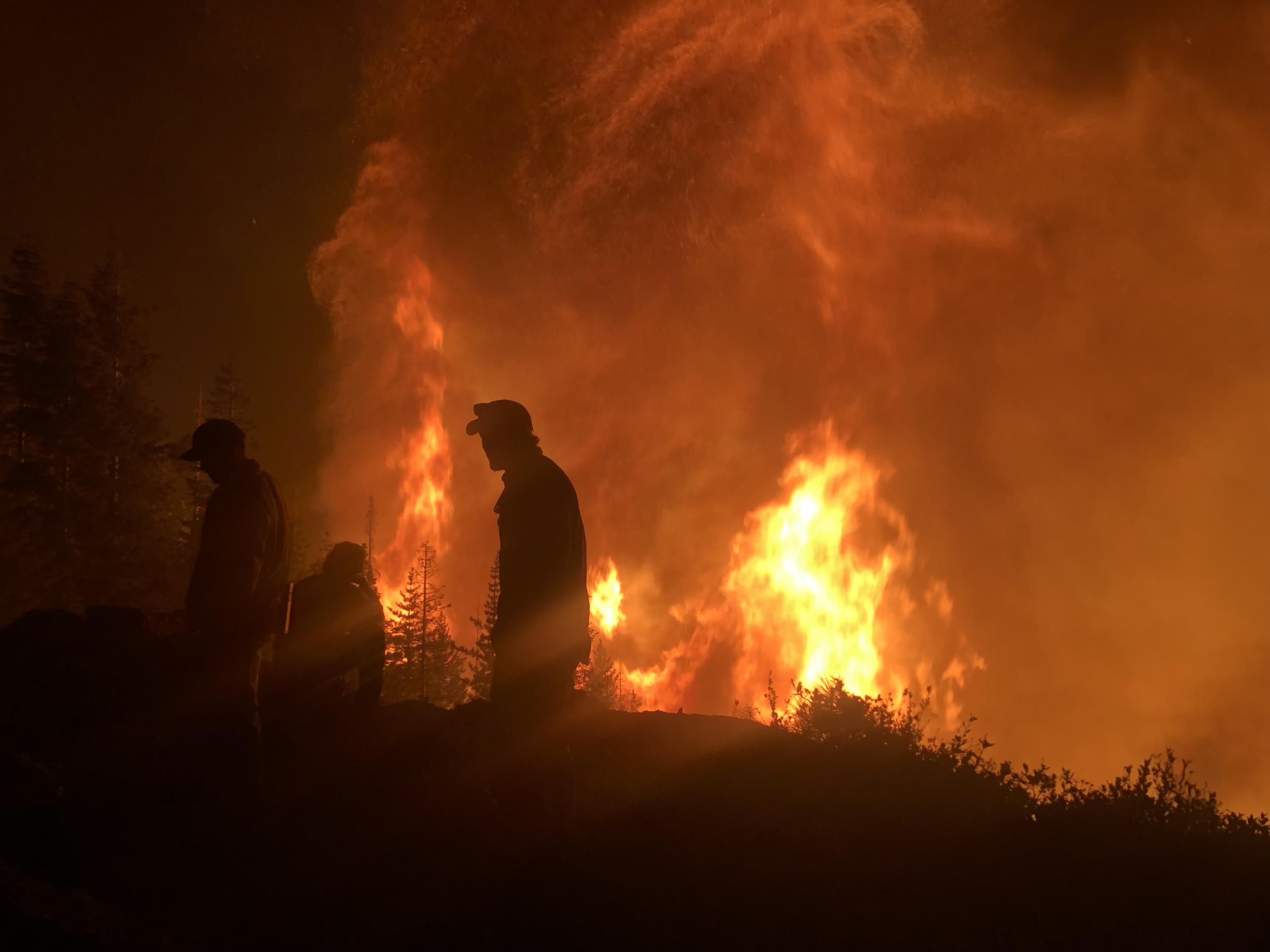 Silhouettes of of three people in the dark as the Deep Fire burns in the distance. 