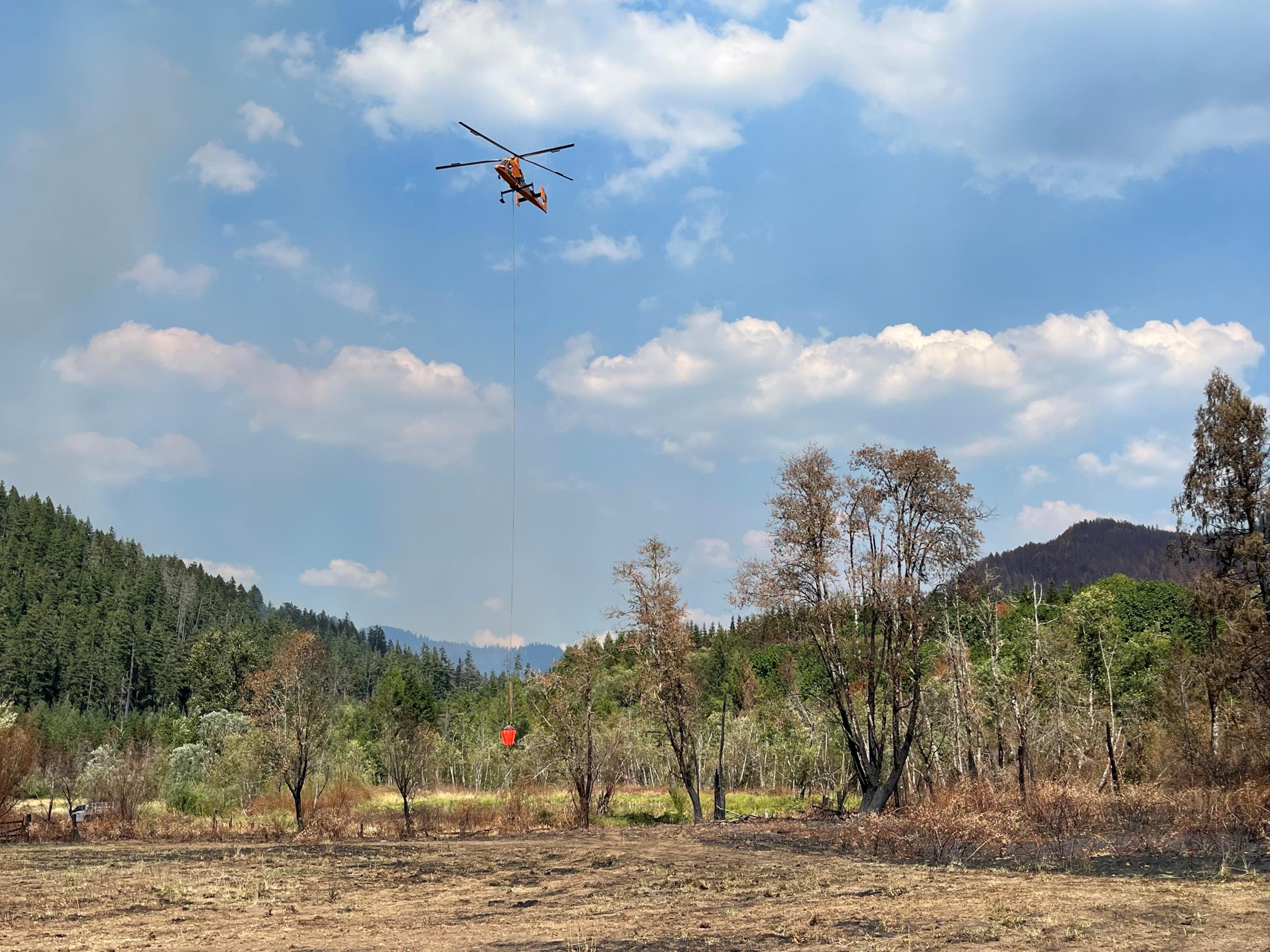 A K-max heavy helicopter at the dipsite filling its bucket to drop water on the active parts of the fire.