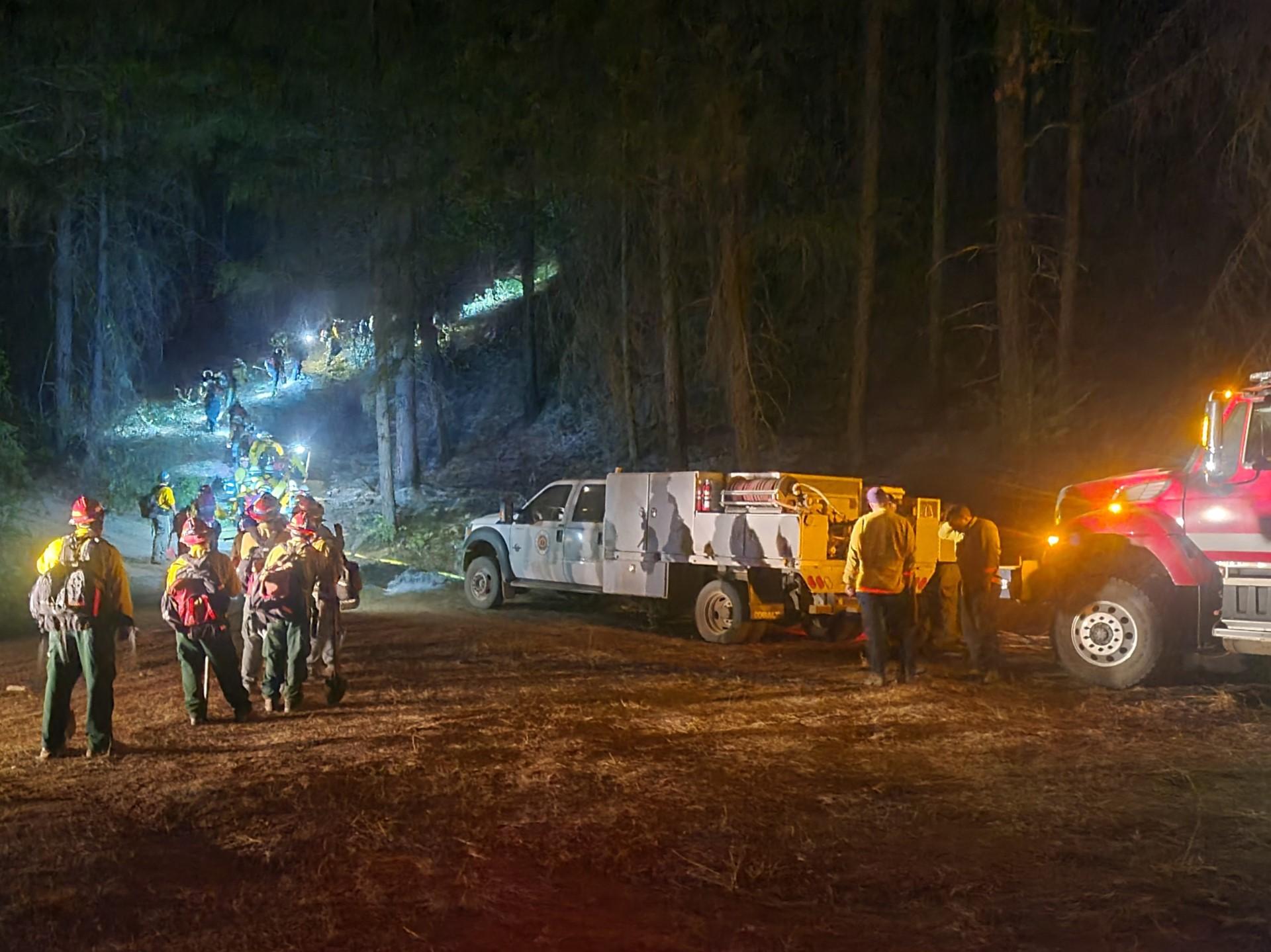 Image of fire crews at night with headlamps walking up a trail into the forest to work on the fire line. Photo USDA Forest Service courtesy Sean Lenzo