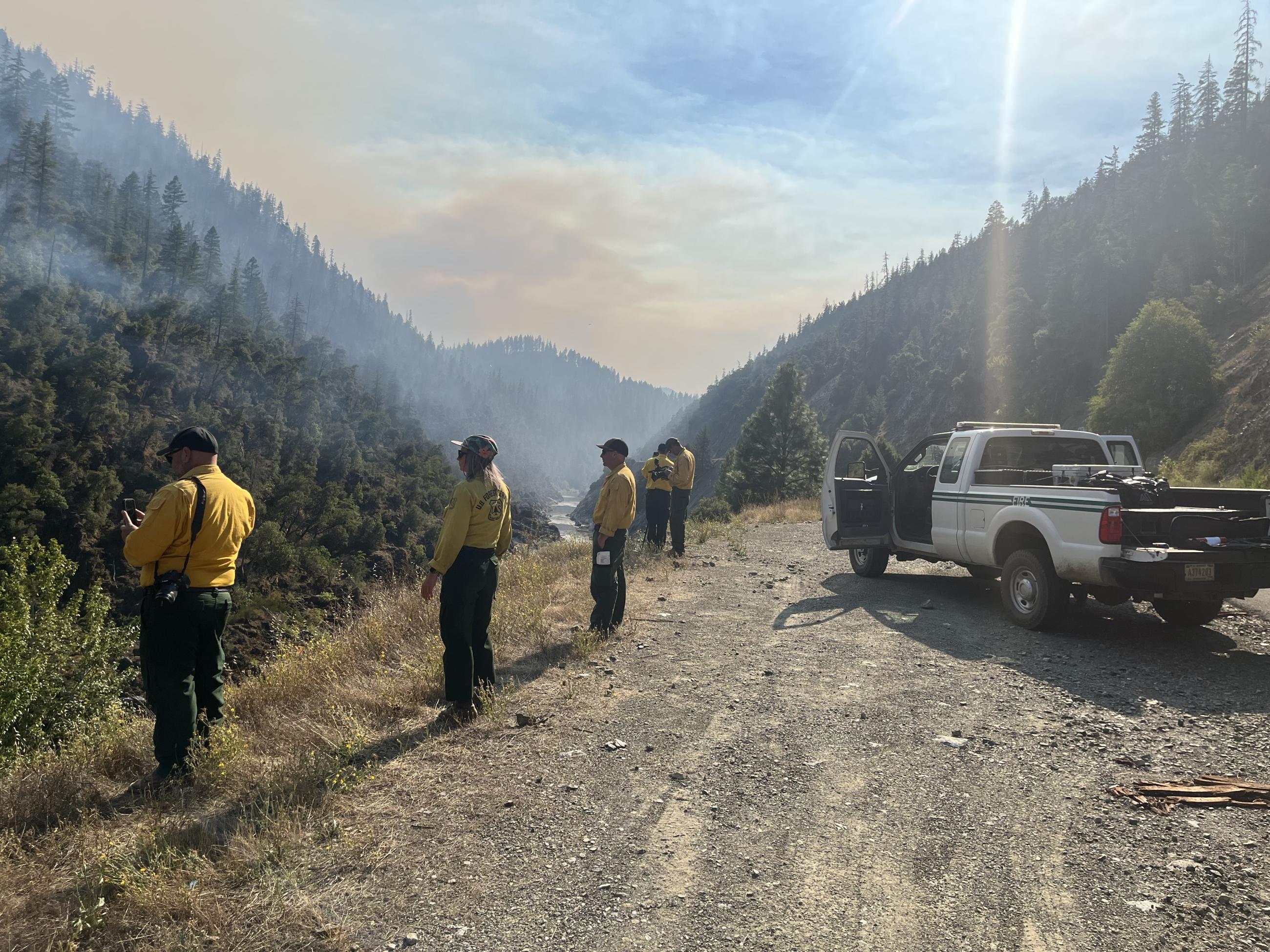 Image of fire officials wearing yellow shirts high above the Klamath River watching firing operations across the river. Photo USDA Forest Service courtesy K. Julian