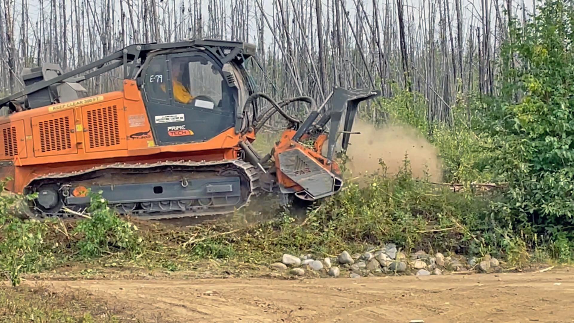 A large yellow tracked masticator removes vegetation as it moves from the left of the photo frame.