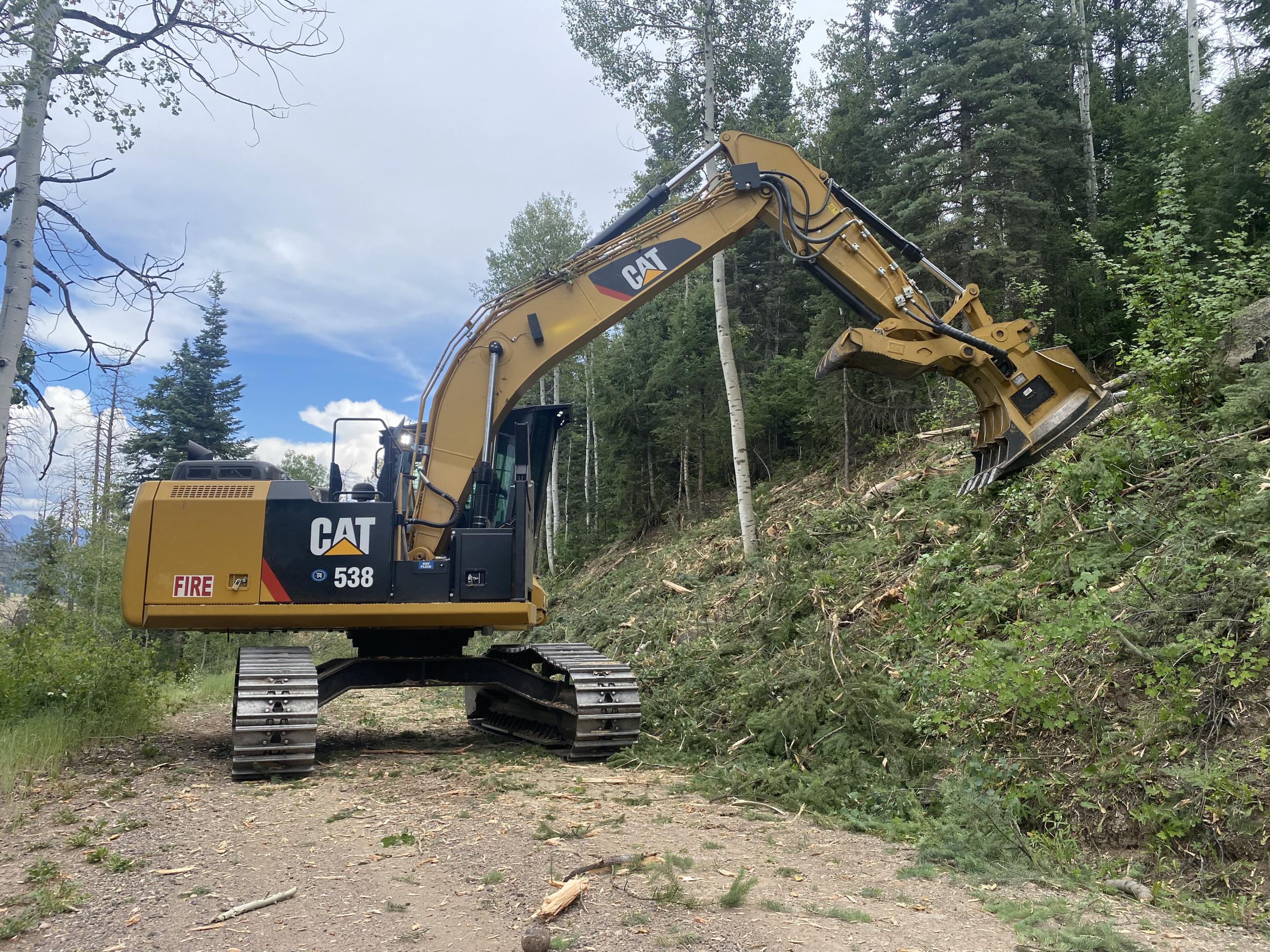 a large masticator grinds vegetation along a road to serve as fireline