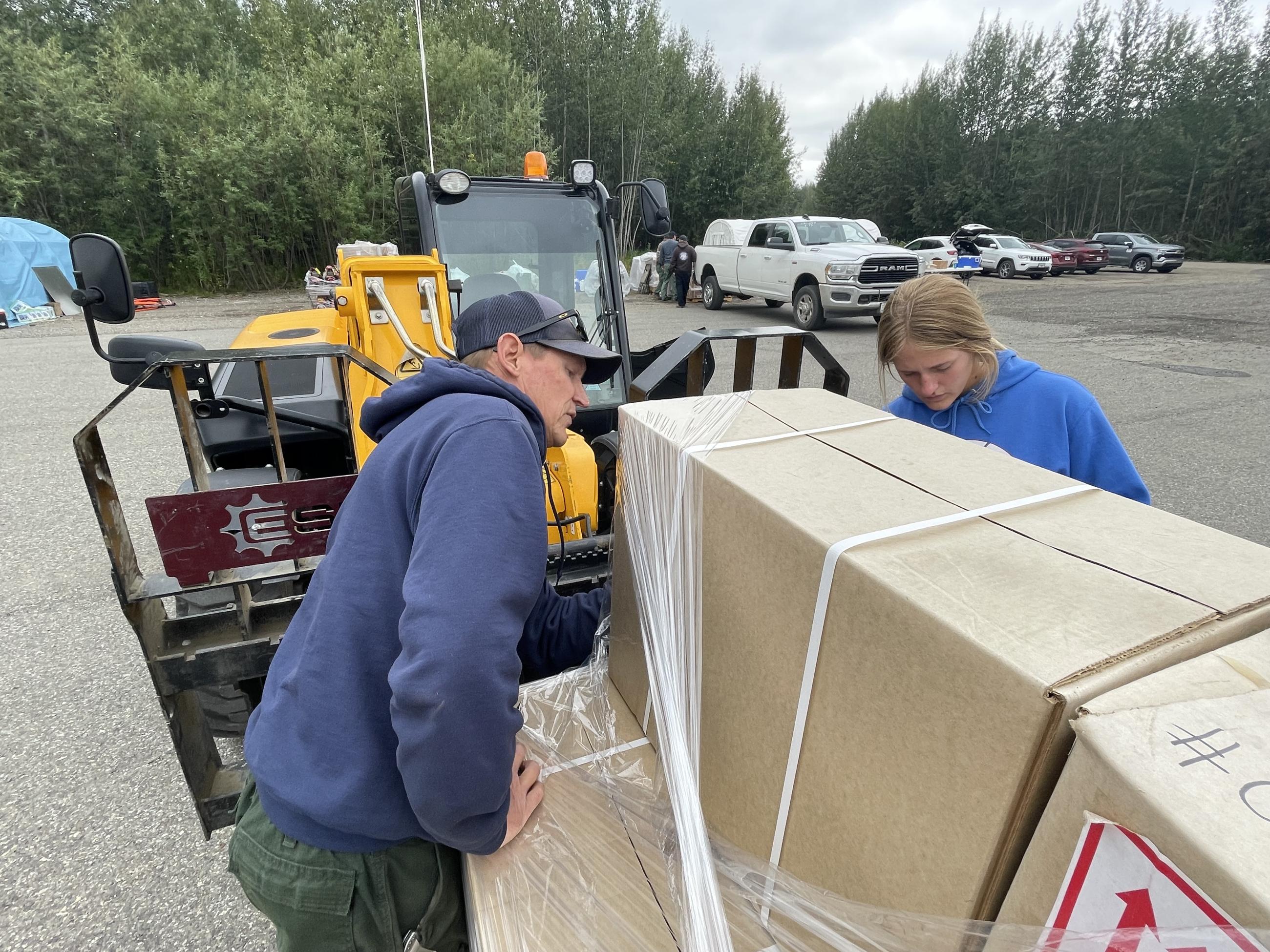 Photo of two logistics personnel in front of a forklift looking at information on boxes on a wrapped pallet