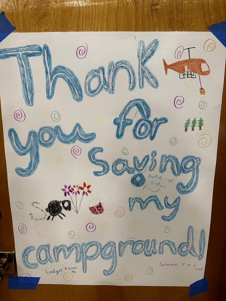 A sign posted by local community members that reads "Thank You for saving my campground" with hand-drawn images of flowers, helicopters, and trees to showcase support for firefighting personnel
