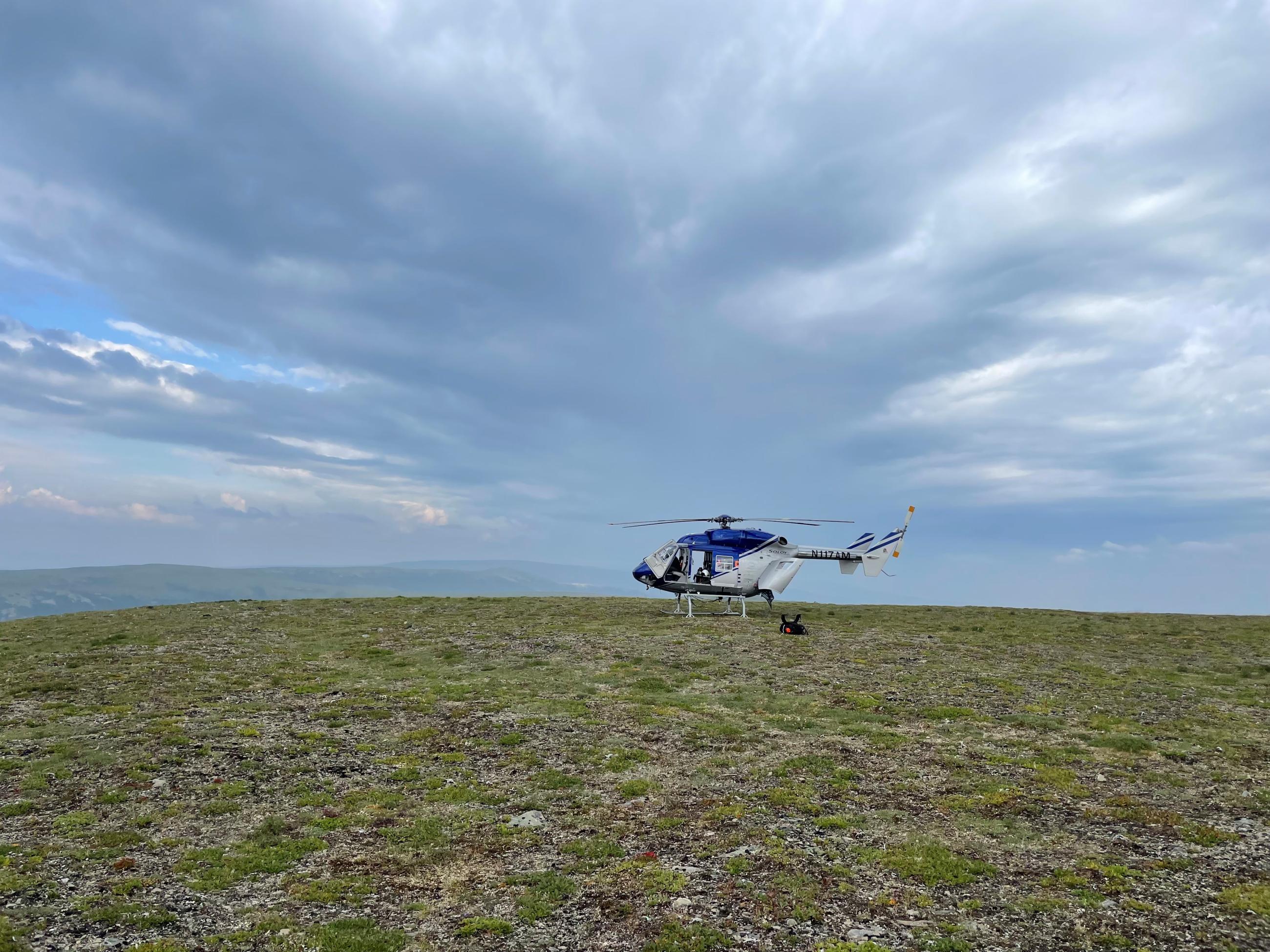 A helicopter on a large field of green with clouds overhead