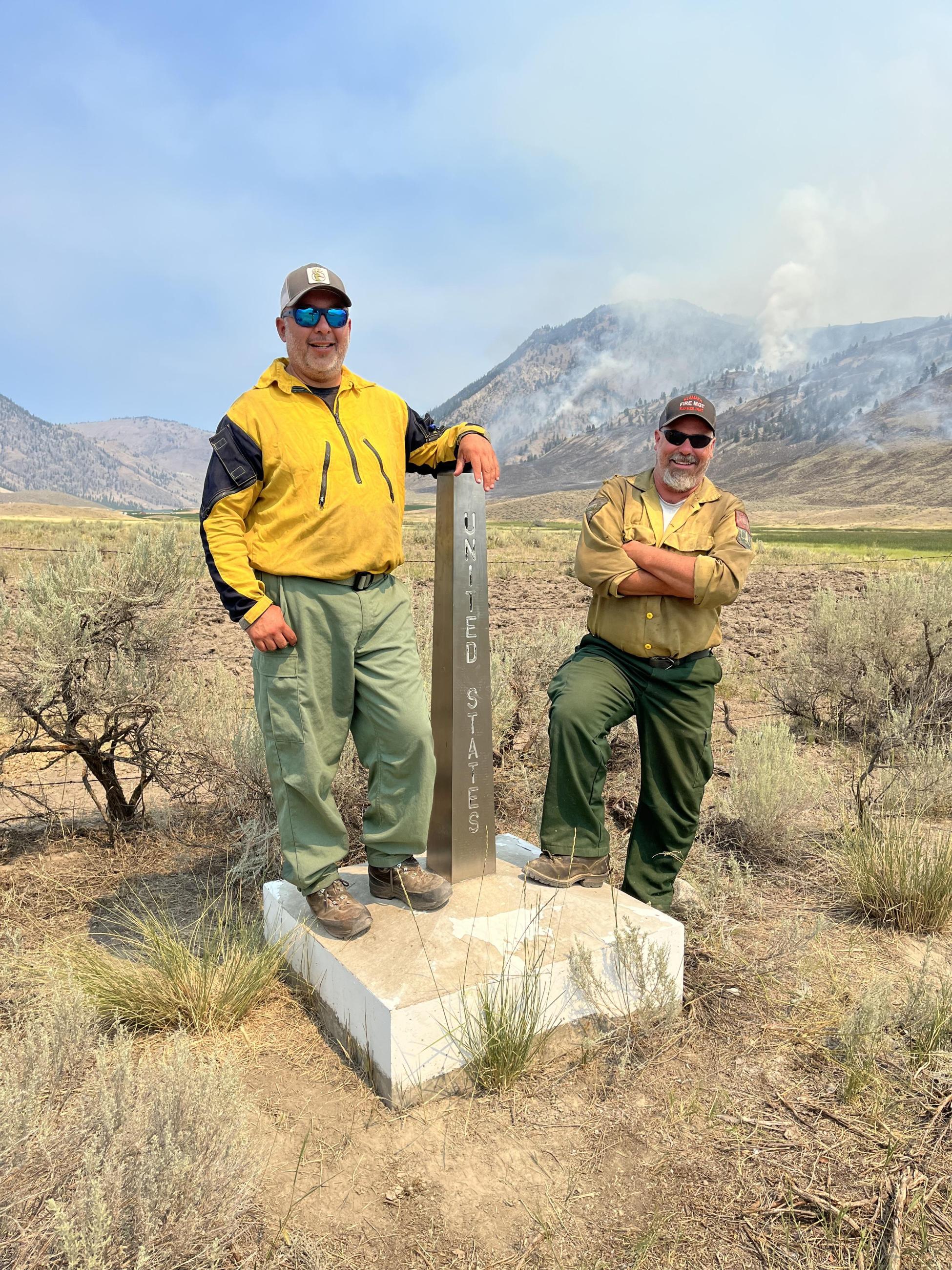 Two firefighters stand next to the United States obelisk on the United States and Canadian Border