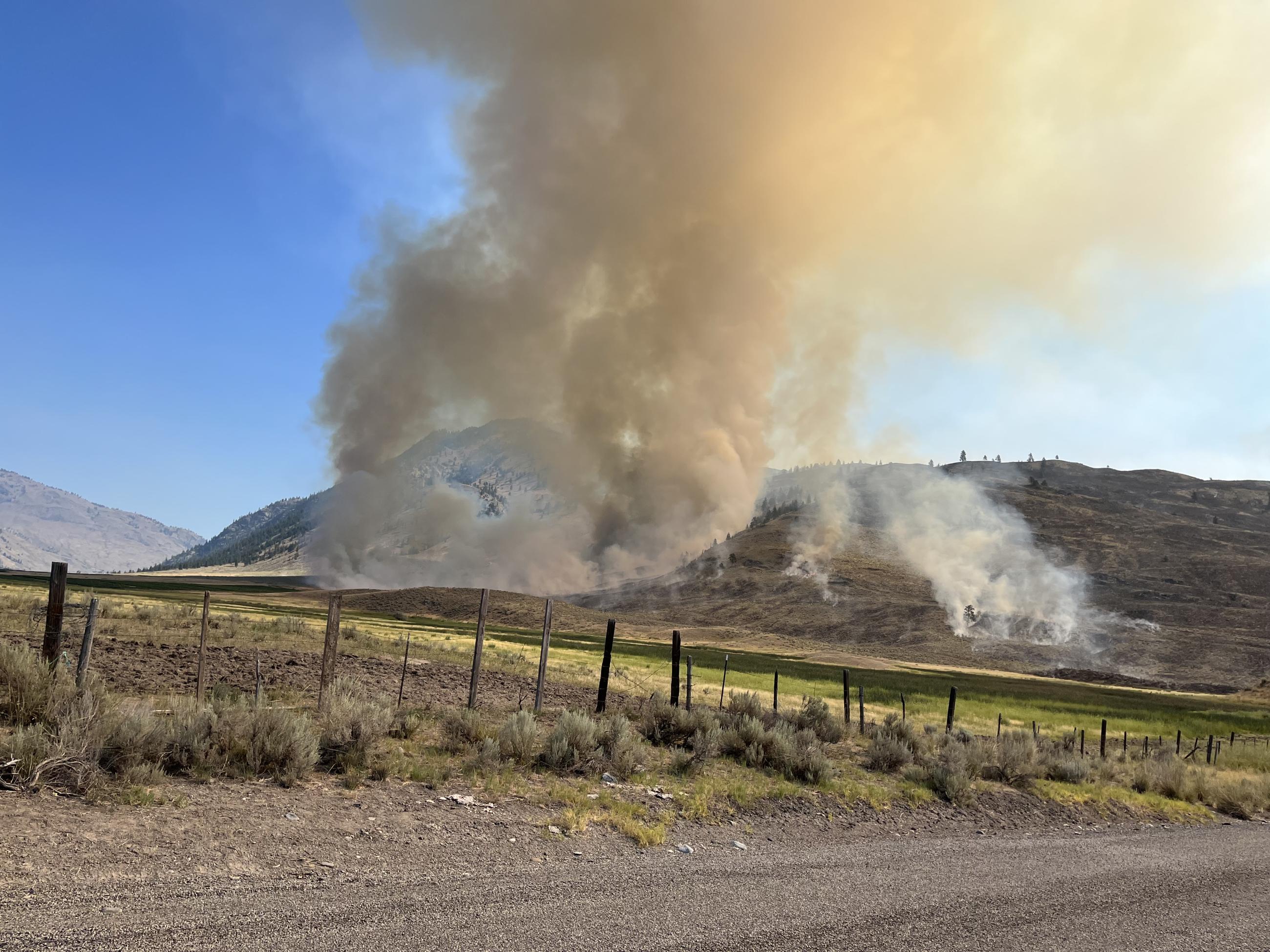 Fire and smoke on a hillside next to a road and fence at the US-Canadian border