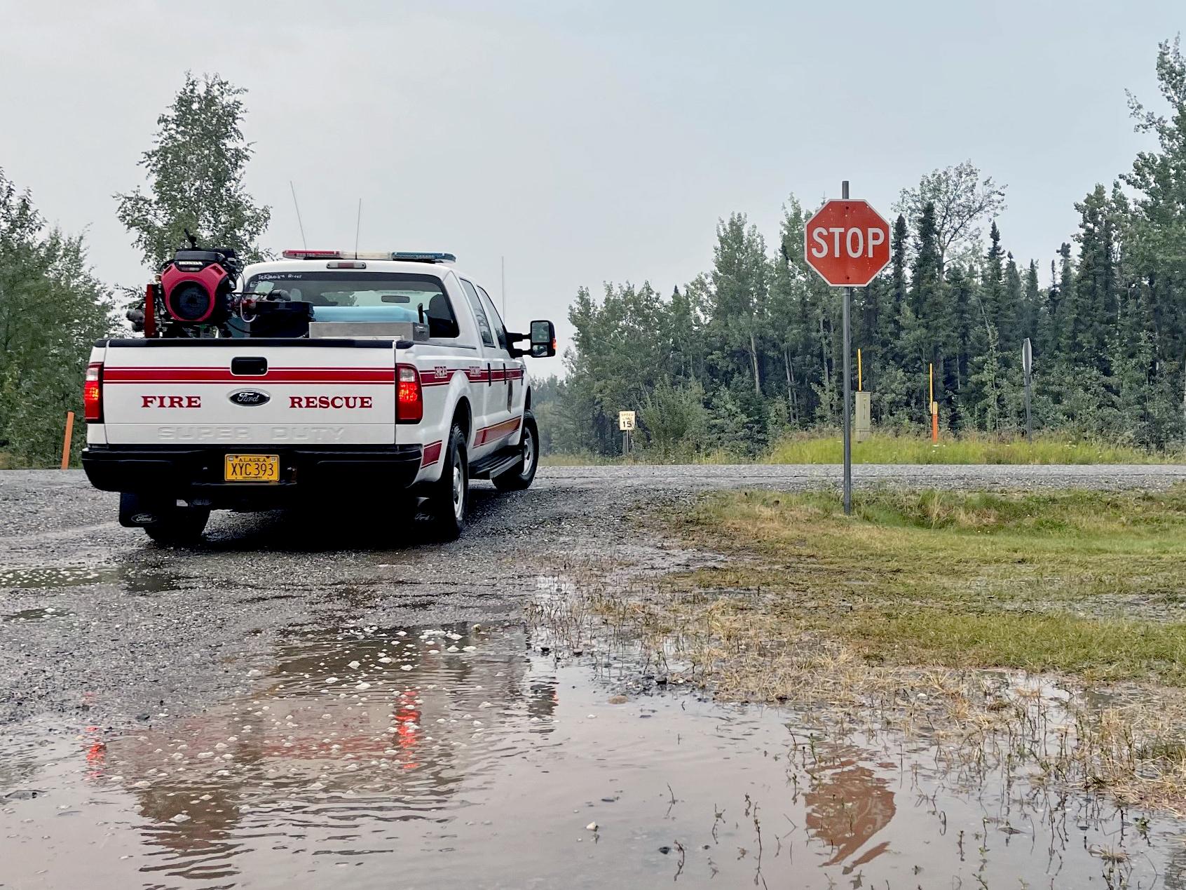 Large puddle in foreground with fire vehicle stopped at a stop sign. Overcast gray skies show the rainy conditions at ICP.