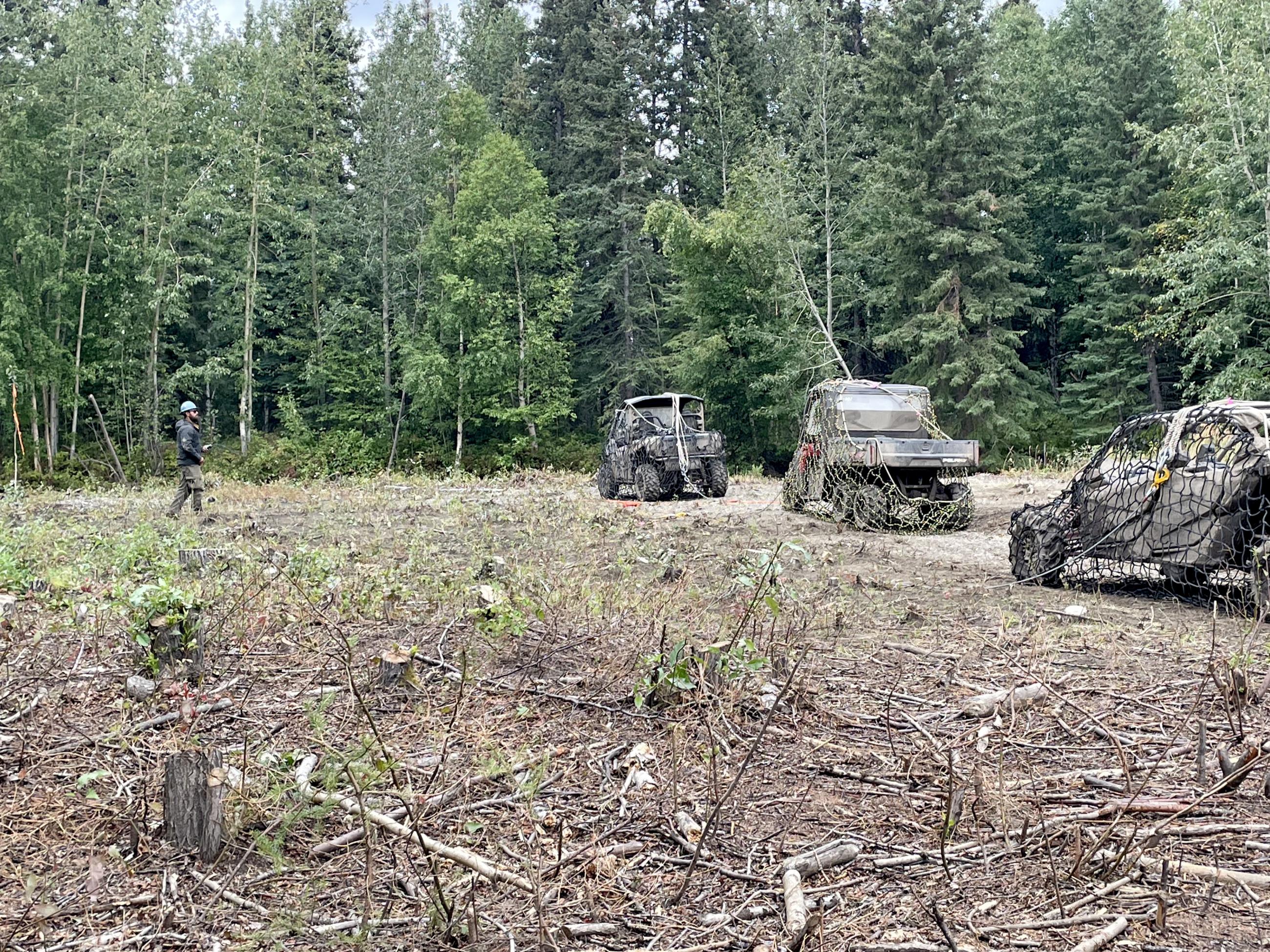 Three UTVs are secured with netting and cables to be airlifted with a long line from a blackhawk helicopter.