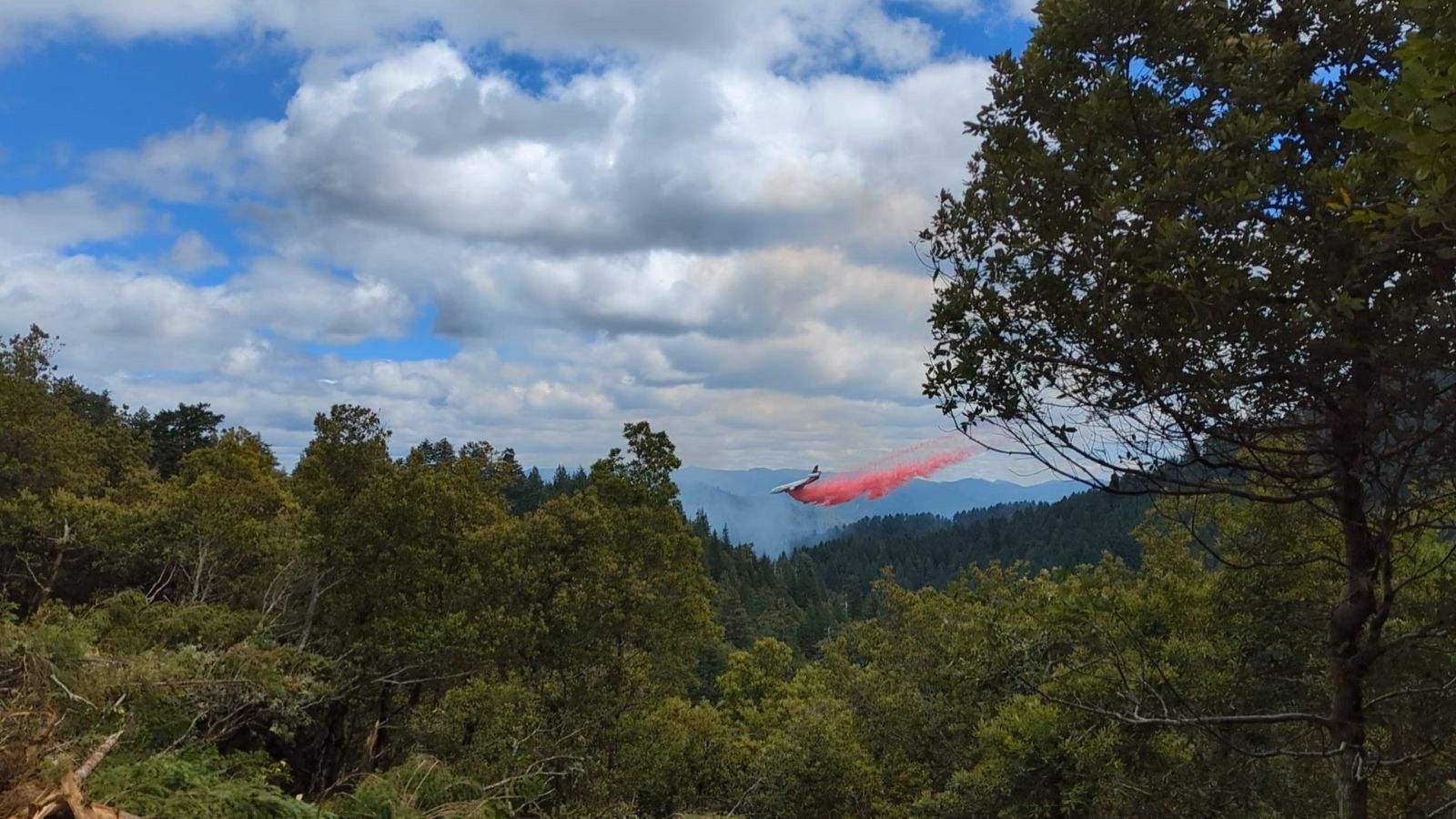 An air tankter drops red retardant over a smoking portion of wilderness. 