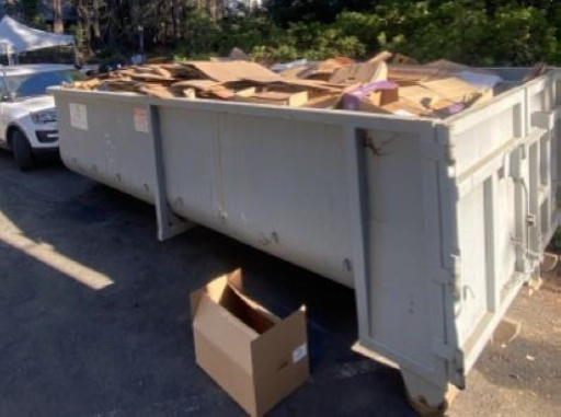 image shows a metal dumpster loaded with flattened cardboard boxes.