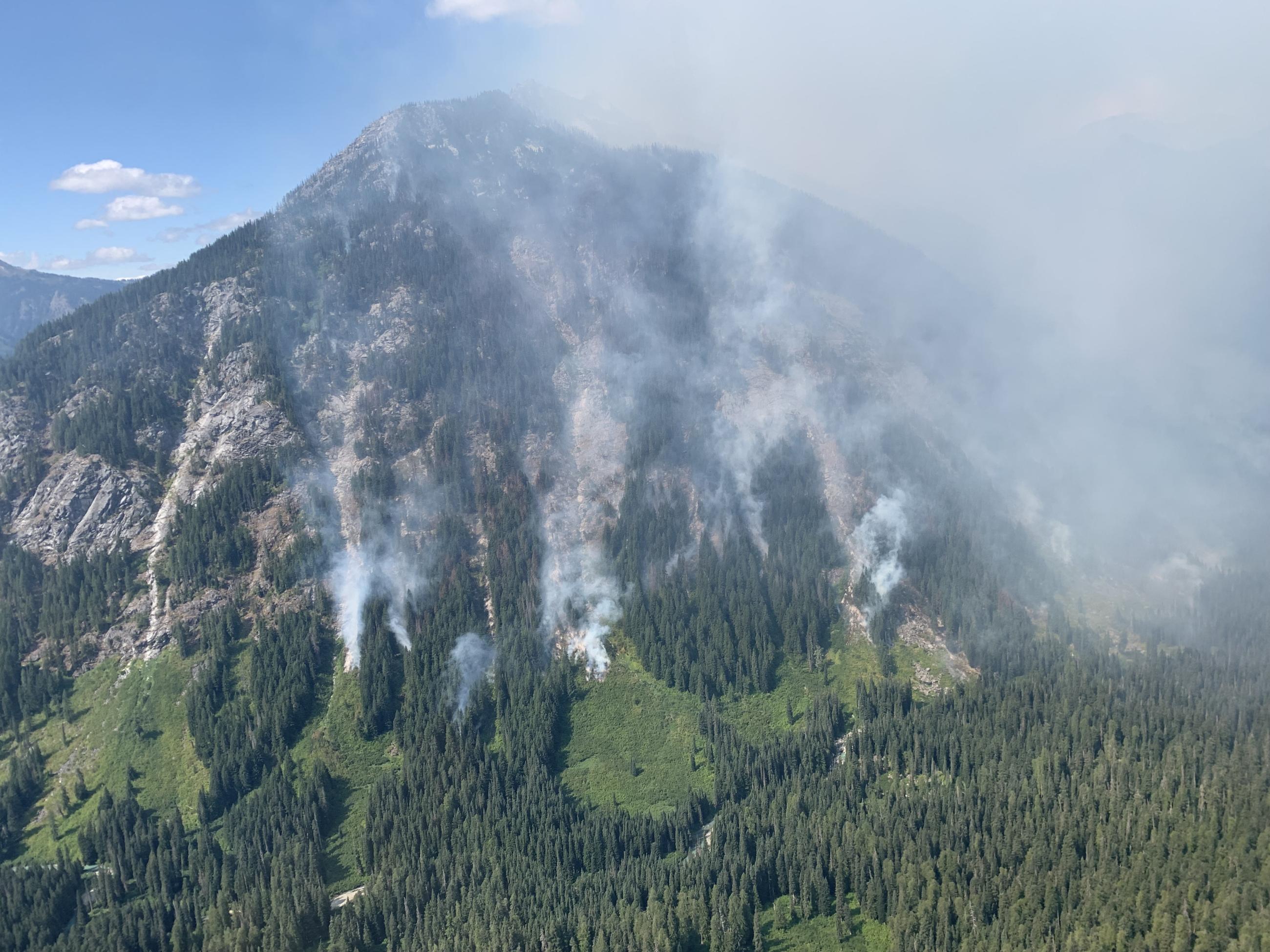 Tendrils of white smoke are visible in three avalanche chutes on a hillside in the Glacier Peak Wilderness Area where the Airplane Lake Fire is burning.