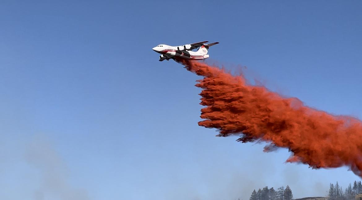 An air tanker drops a load of orange retardant across the fire line
