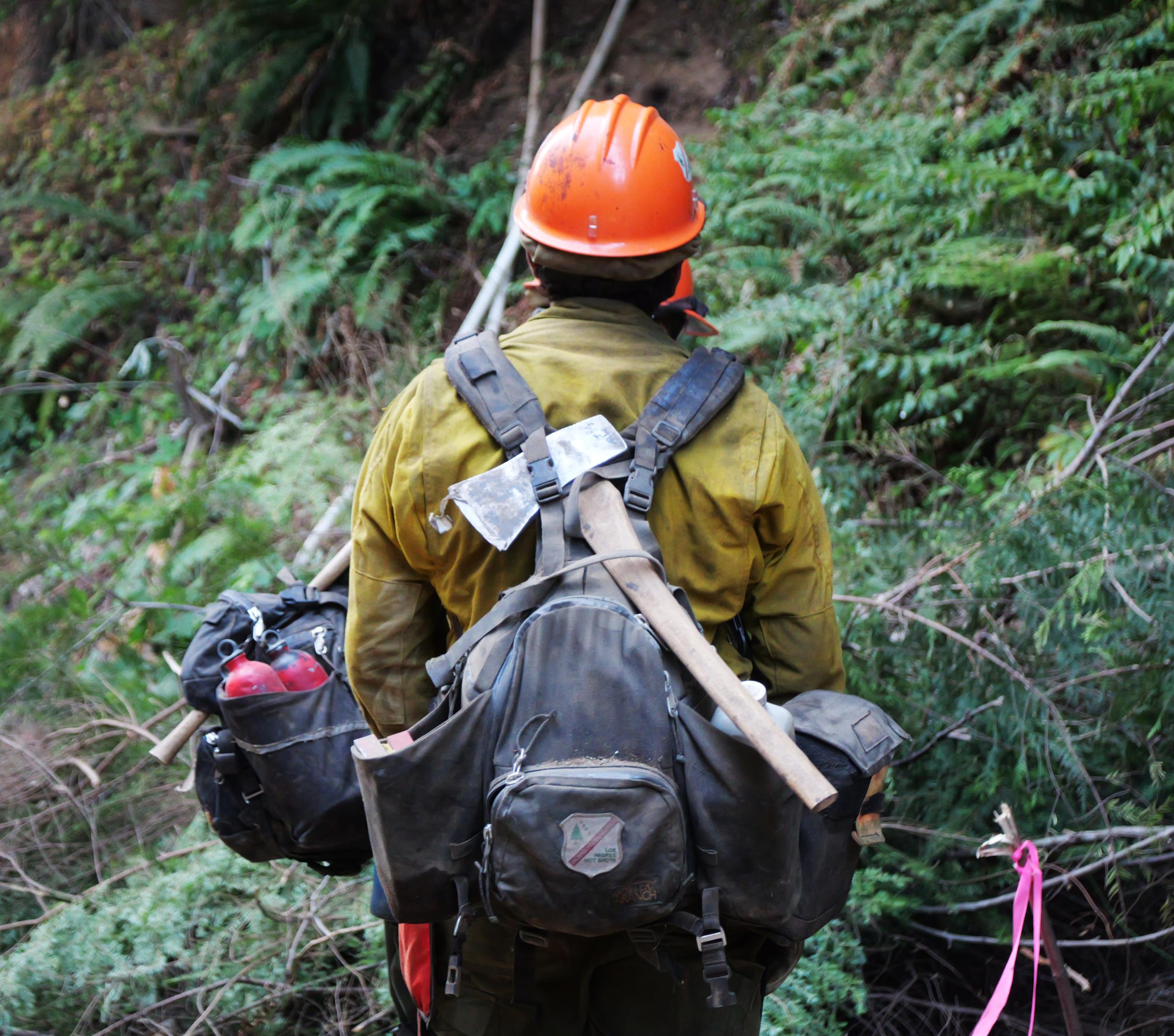  A firefighter with an orange helmet and a small axe hanging off his pack watches for "spot fires." 
