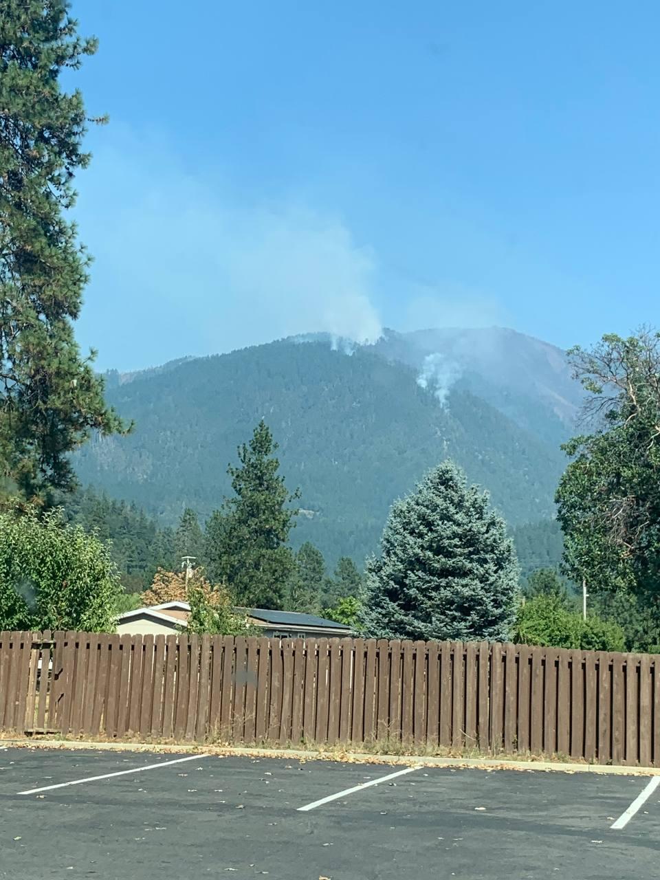 Two plumes of smoke rising from the mountains as seen from the Orleans Clinic with a fence in the foreground