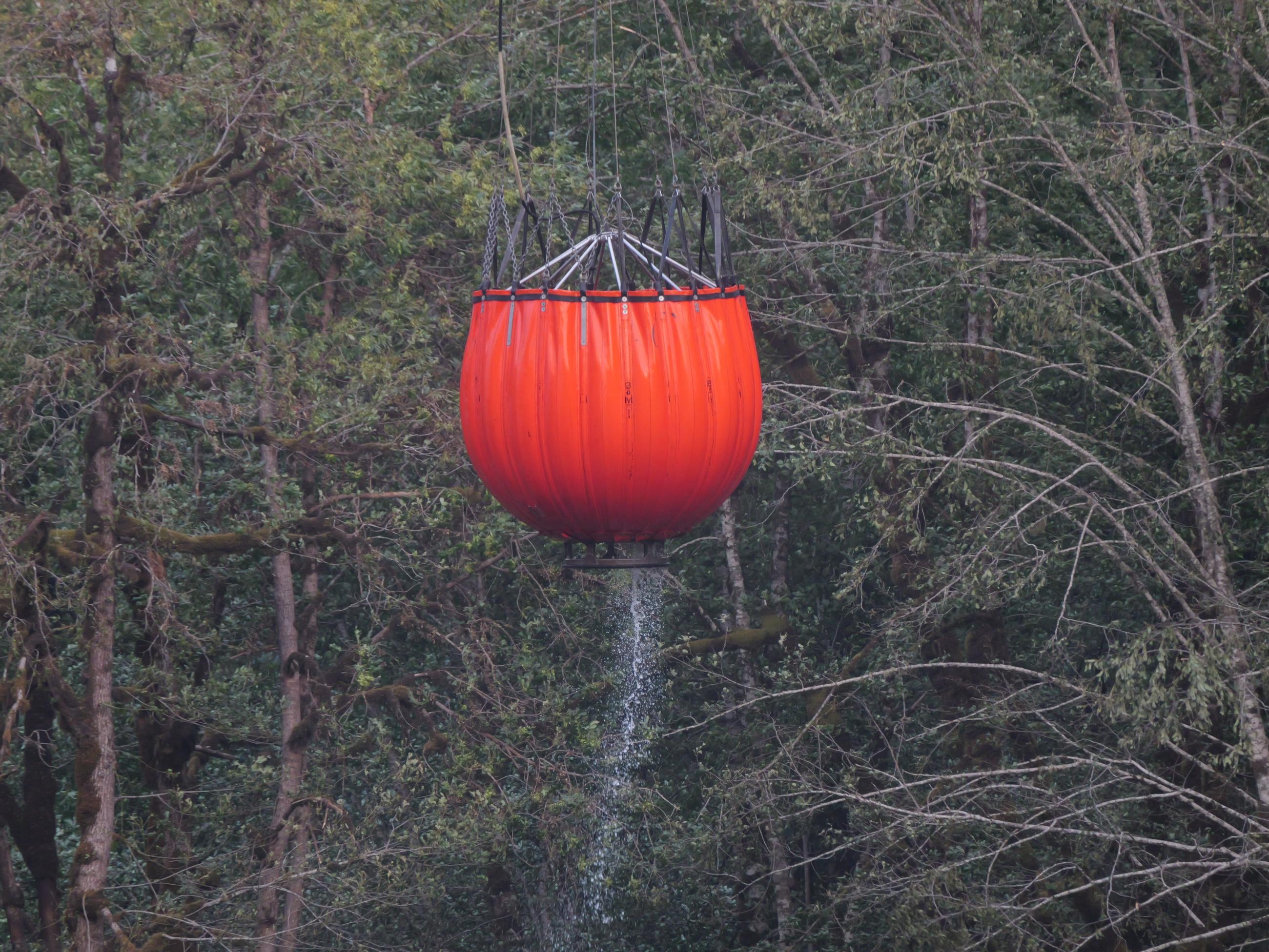 A "bambi" bucket drips water as it is lifted by a helicopter.