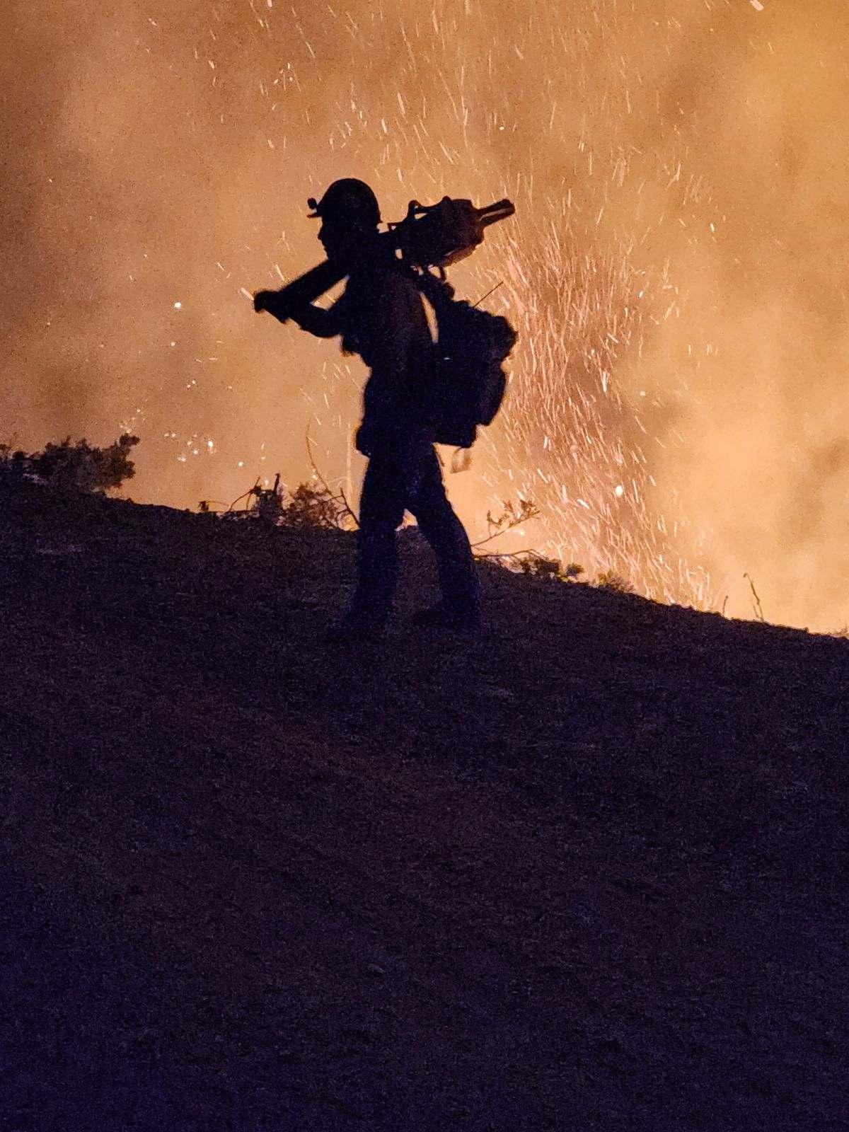 Silhouette of a firefighter carrying a chainsaw with glowing smoke behind. 