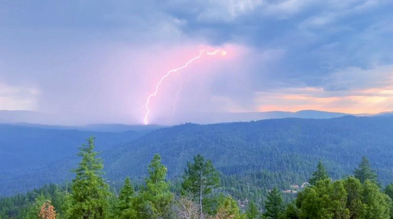 A thunderstorm and lightning are visible over forested hills.