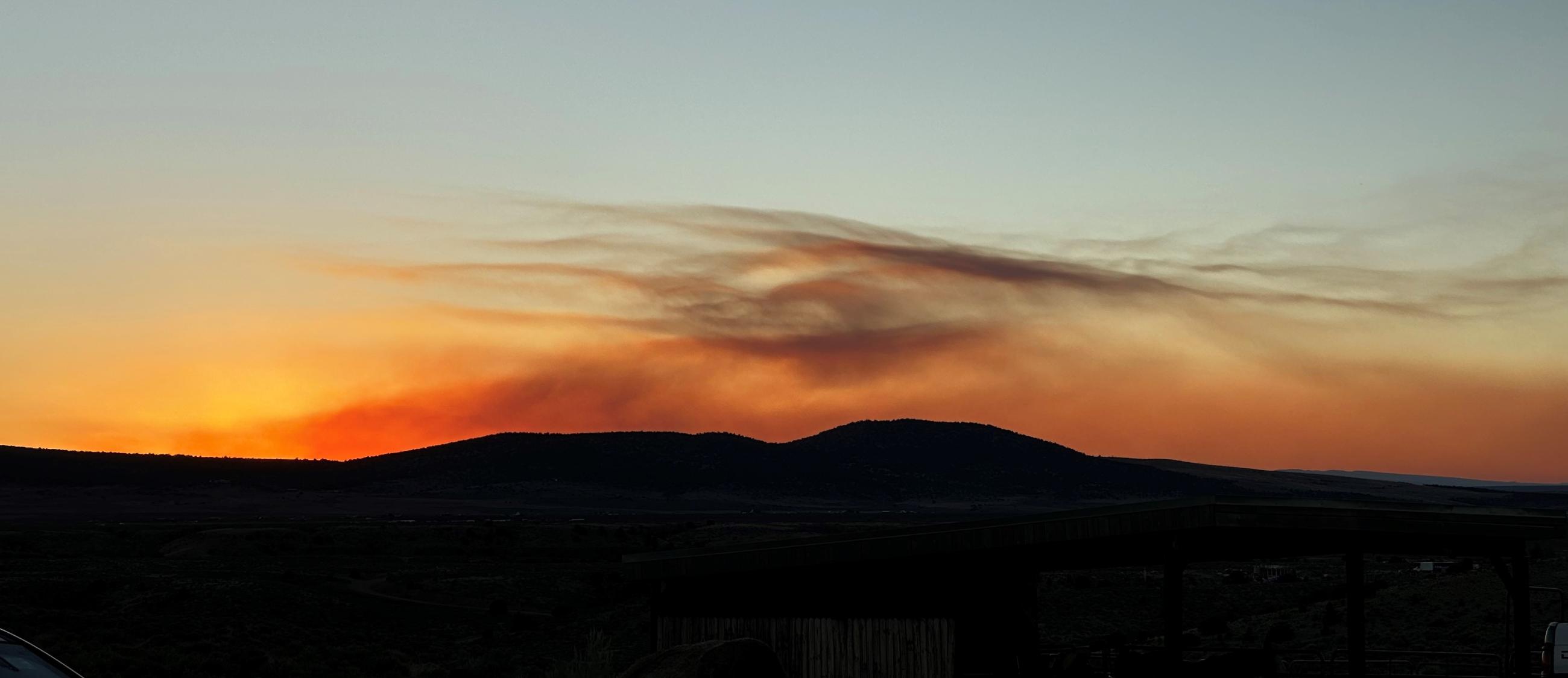 Smoke rises behind silhouetted hills at sunset.