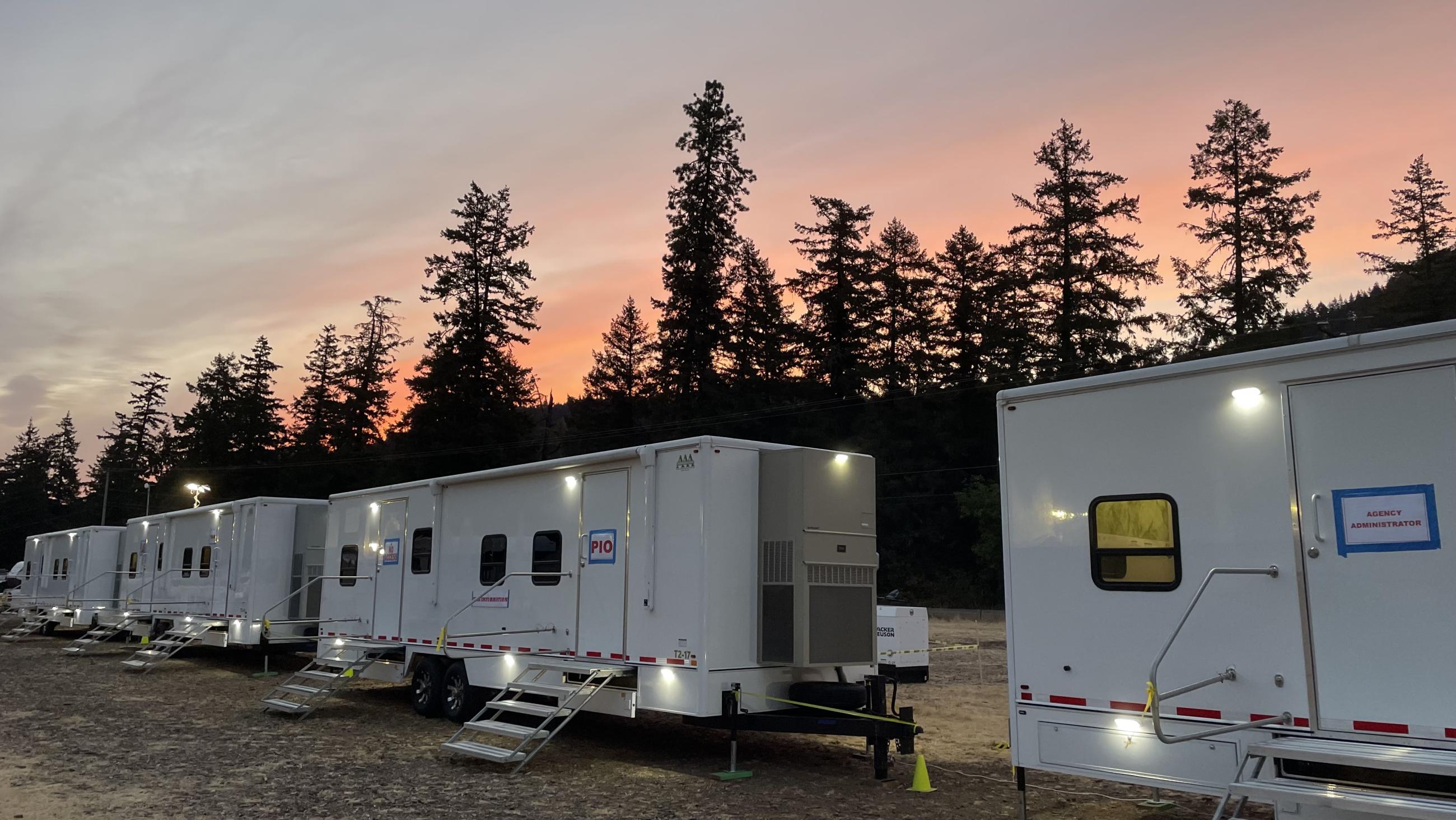 White trailers in front of a pink sunset and green trees