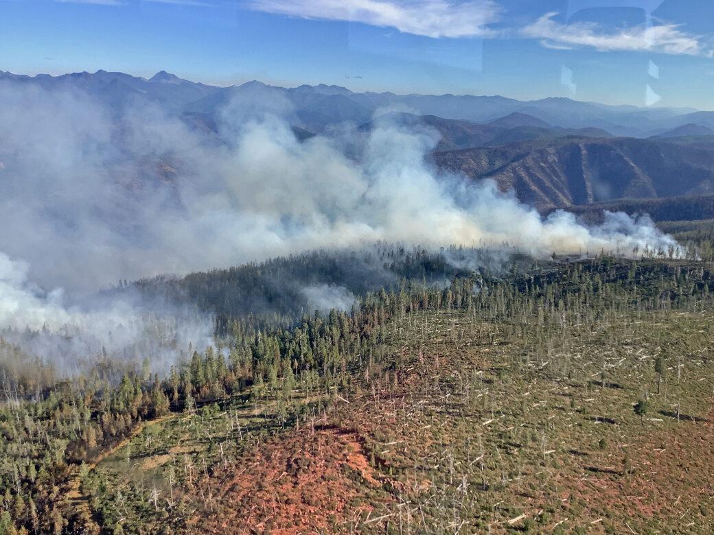 Lines of smoke rising from a ridge adjacent to an old fire scar.