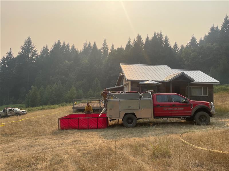 a red fire truck is parked in front of a cabin near a square, open above-ground pool of water