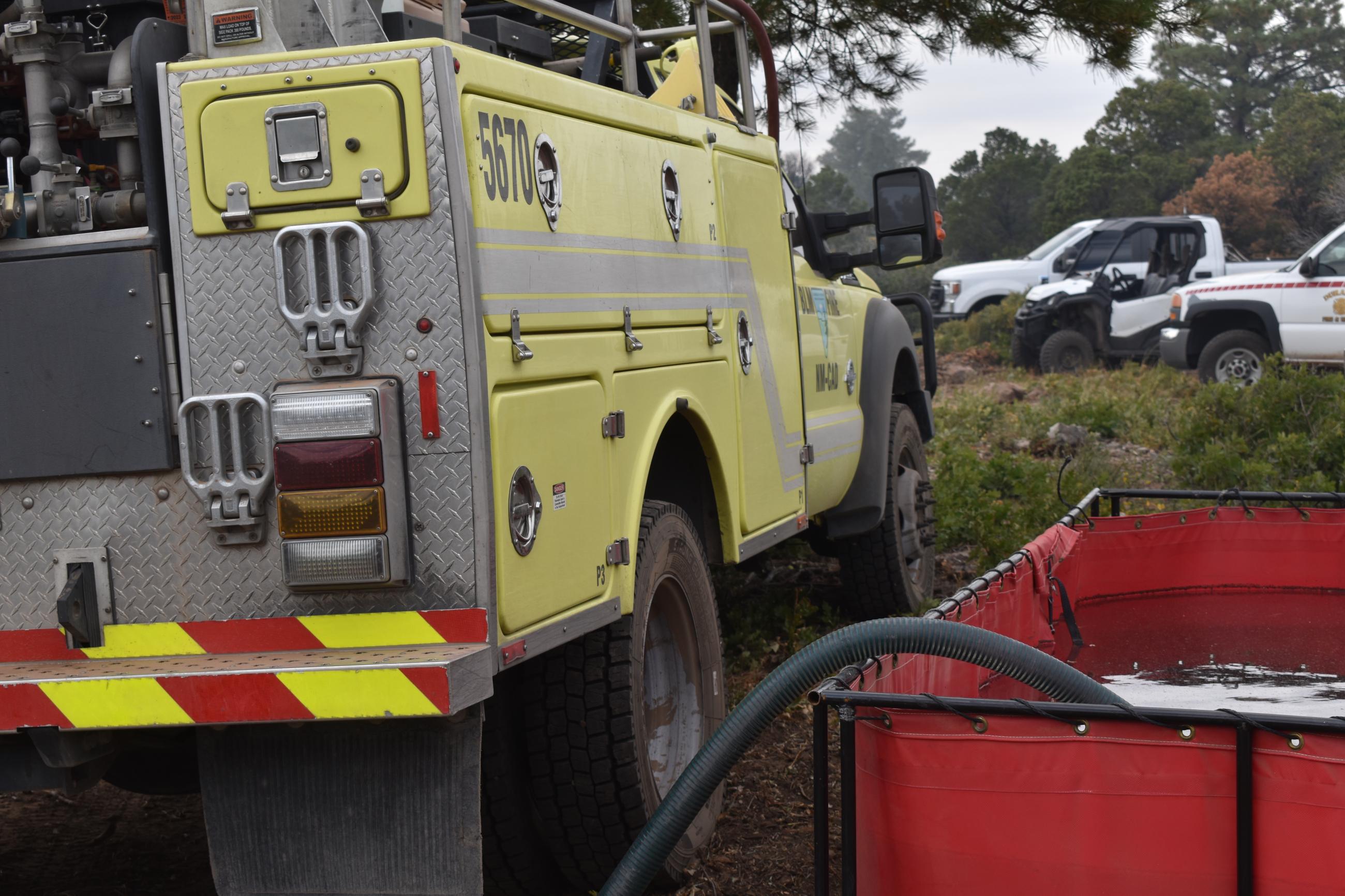 Image of BLM fire engine, portable water tank with draft hose, other fire vehicles. 